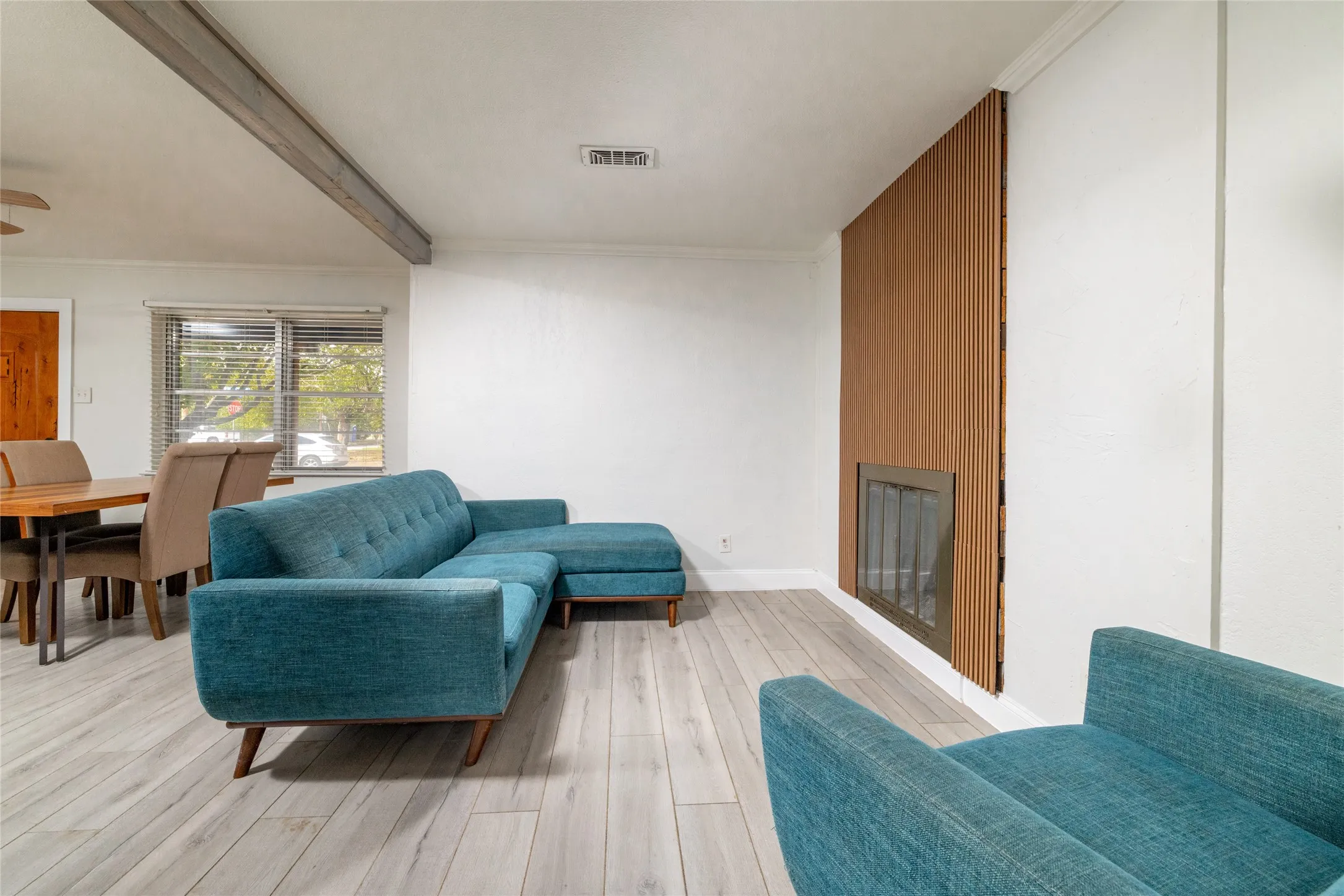 Wood-finish flooring, exposed ceiling beam, and a fireplace with a wood-paneled surround