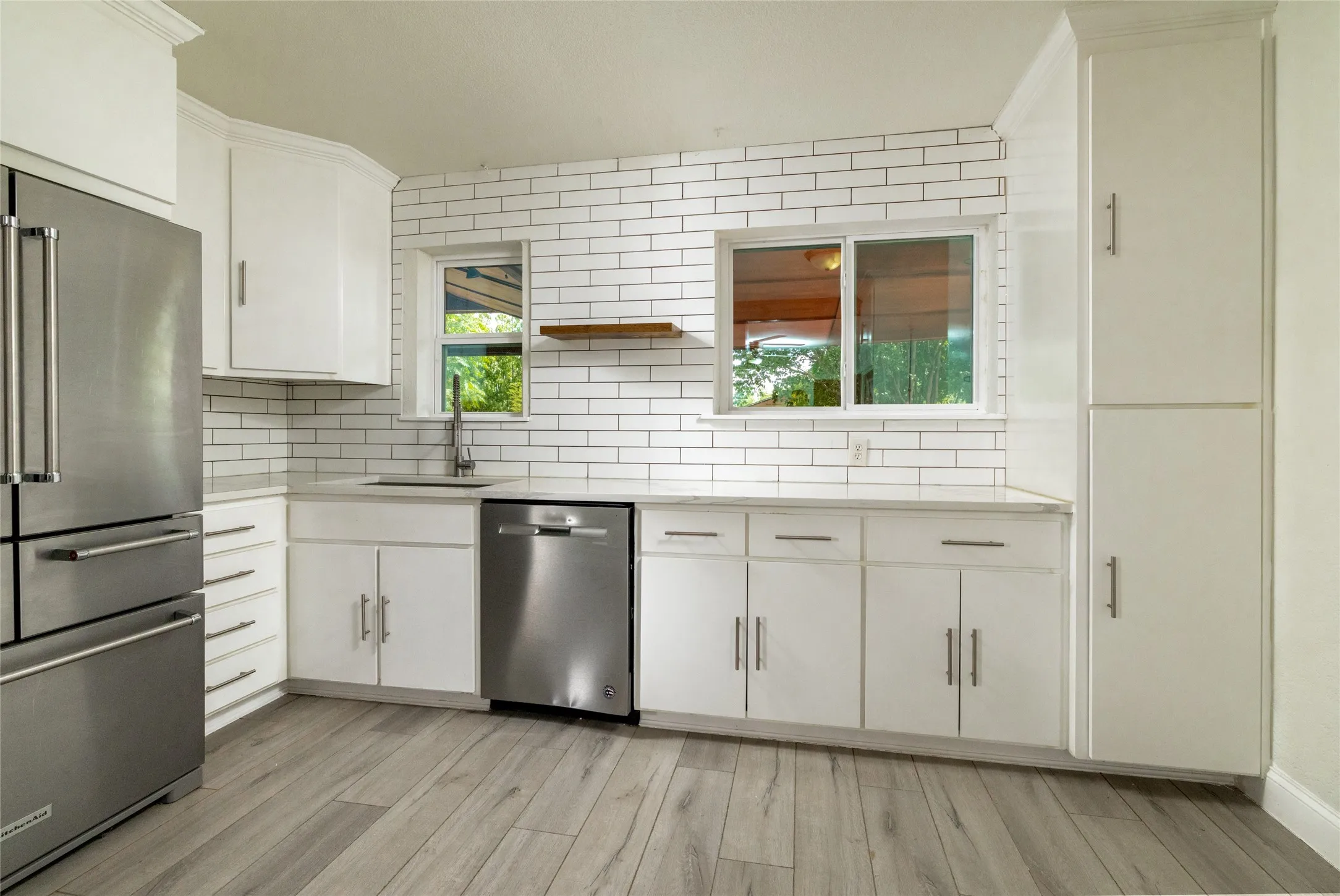 Kitchen featuring white cabinetry, subway tile backsplash, stainless steel appliances, and wood-finish flooring