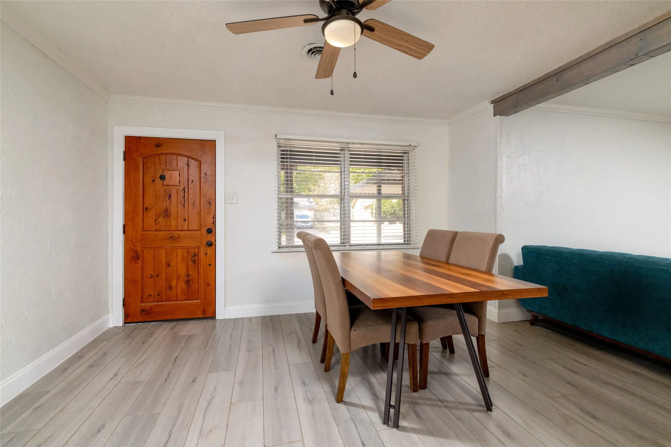 Wood-finish flooring throughout, featuring a wood-panel door with an arched top, a window with blinds, and a ceiling fan