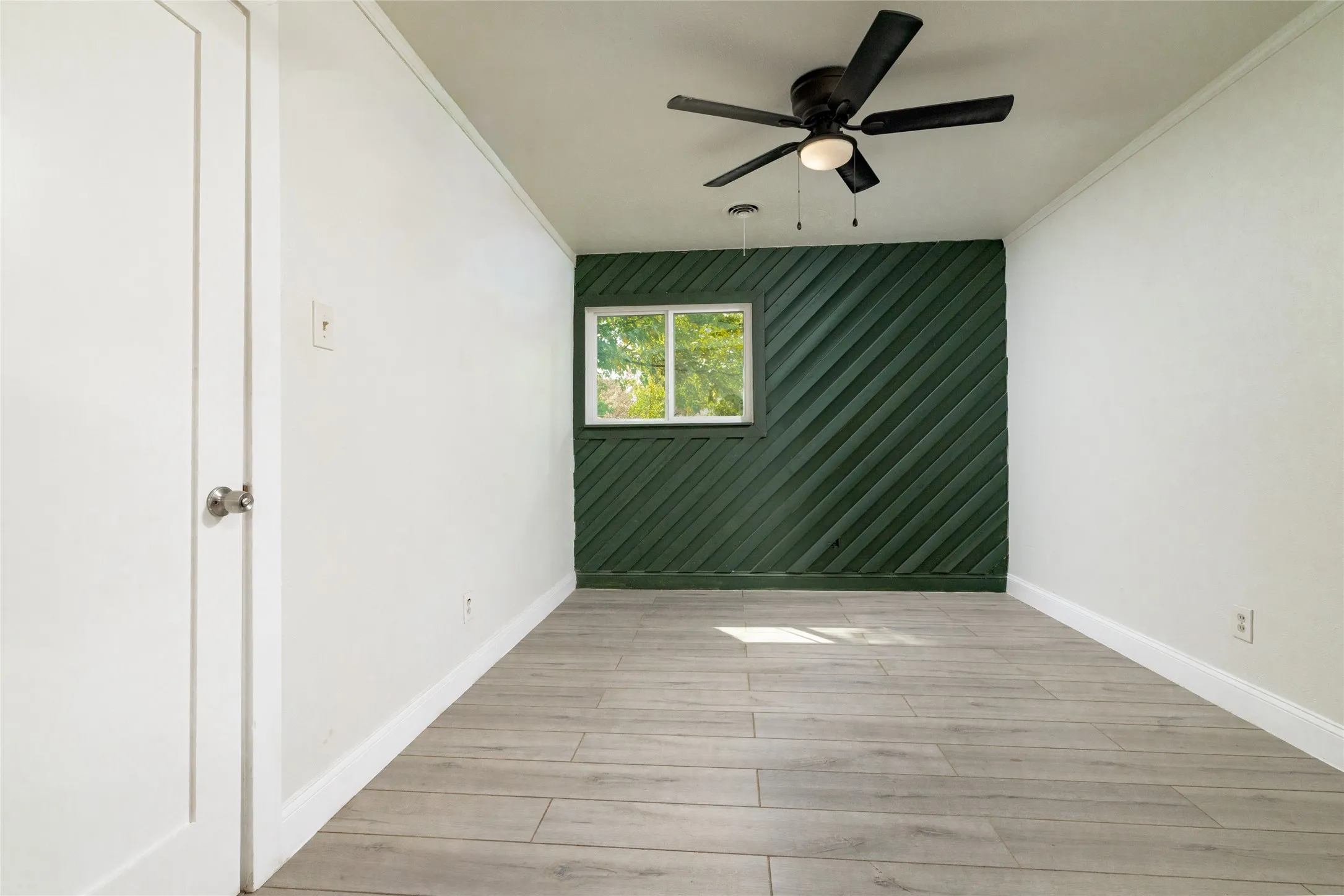 Wood-finish flooring, accent wall with diagonal paneling, ceiling fan with integrated lighting, recessed window, and white trim throughout
