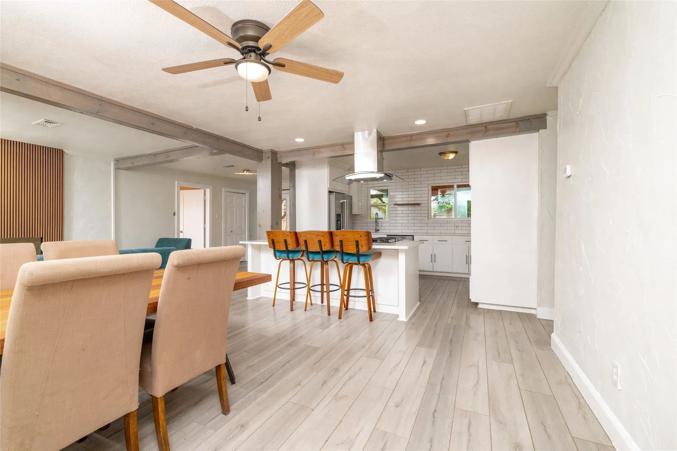 Wood-finish flooring throughout, featuring exposed ceiling beams, a ceiling fan with light, and a kitchen island with seating