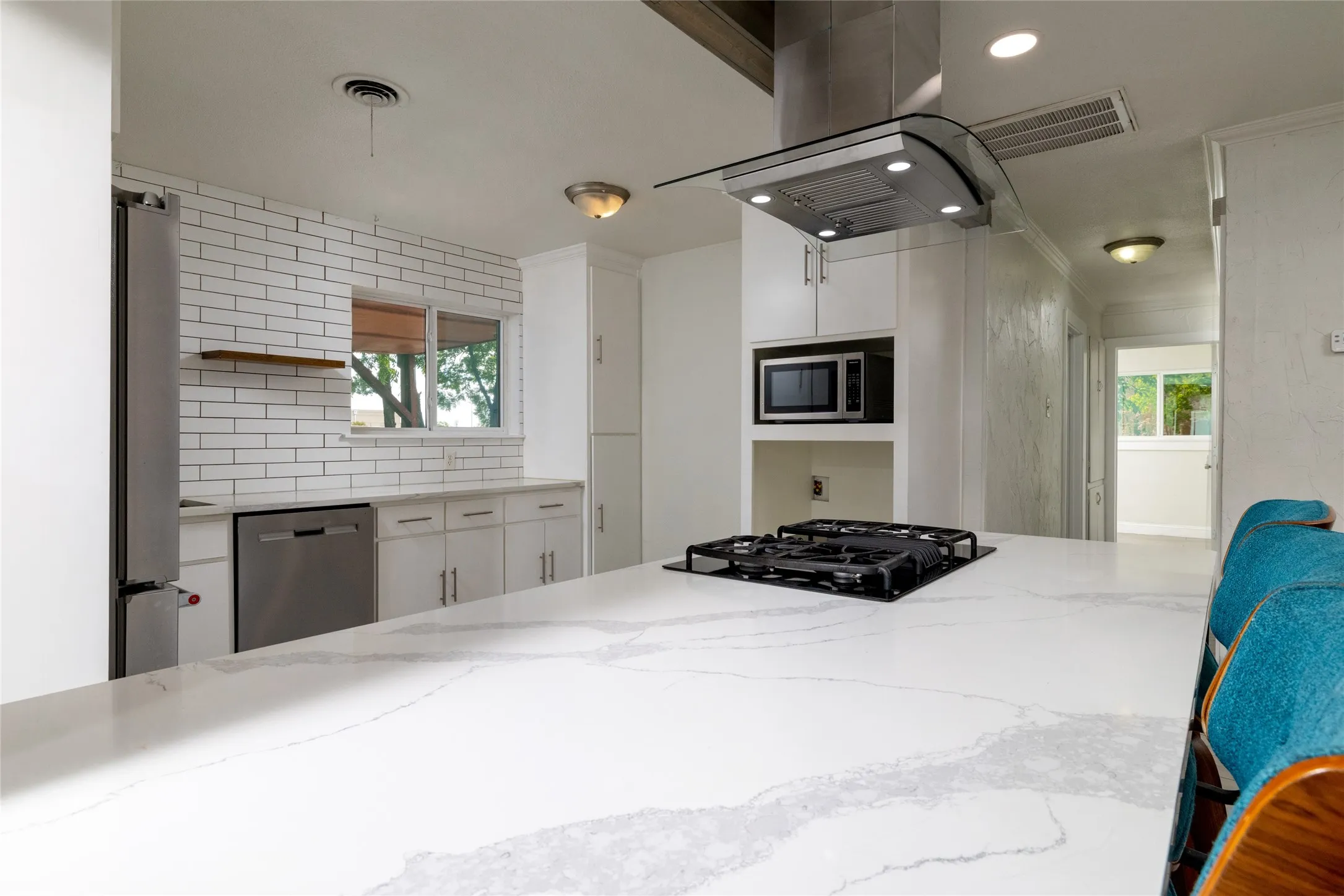 Kitchen featuring a built-in cooktop, stainless steel range hood, stone countertops, white subway tile backsplash, and white cabinetry