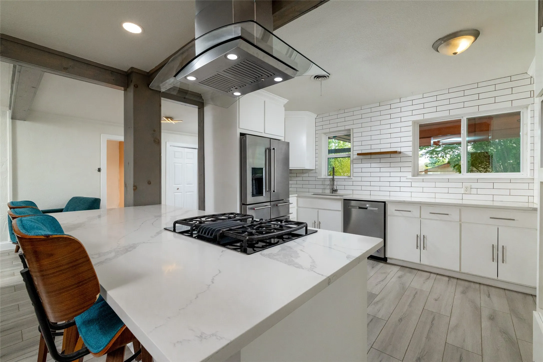 Kitchen featuring a center island with built-in gas cooktop, stainless steel range hood, full subway tile backsplash, wood-finish flooring, and white cabinetry