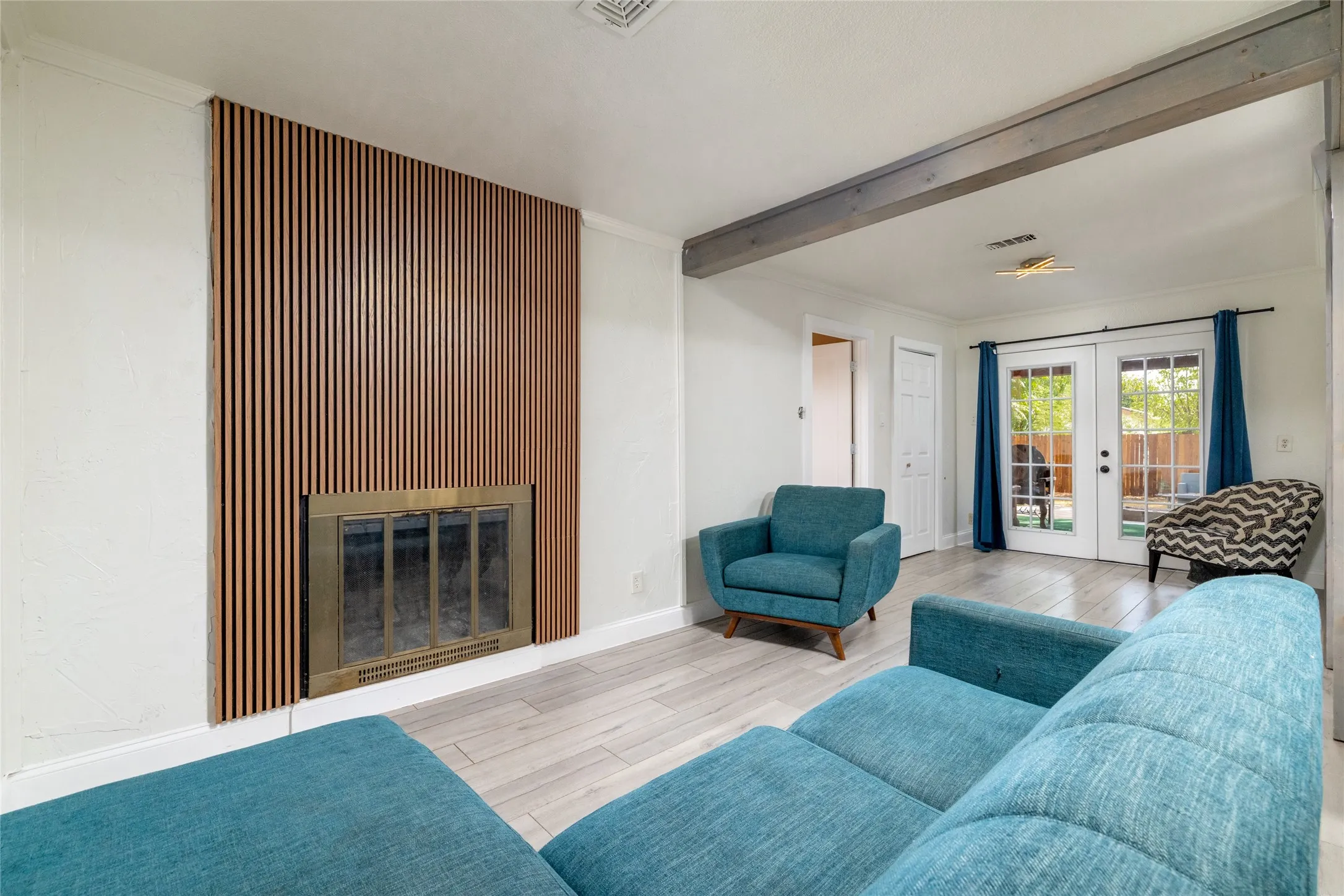 Fireplace with a slatted wood-finish surround, wood-finish flooring, exposed ceiling beam, and double French doors with transom windows