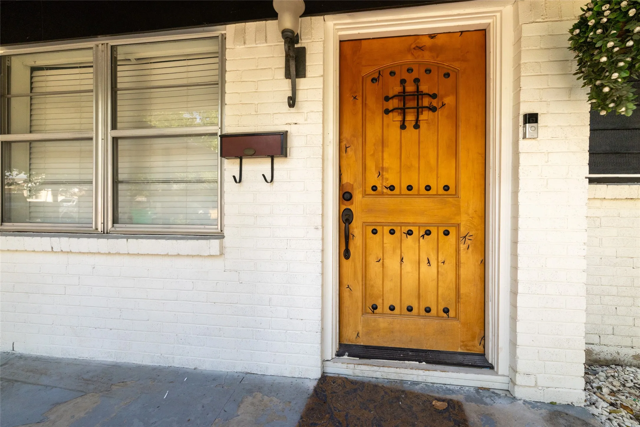 White painted brick exterior with a wood-finish entry door, decorative iron grille, and brushed metal hardware