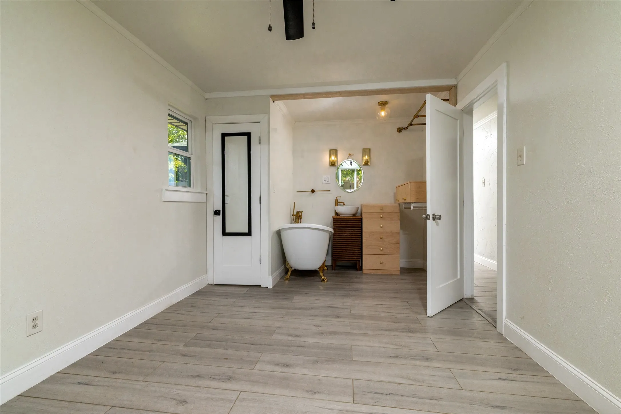 Light wood-finish flooring throughout, white baseboards, and a freestanding soaking tub