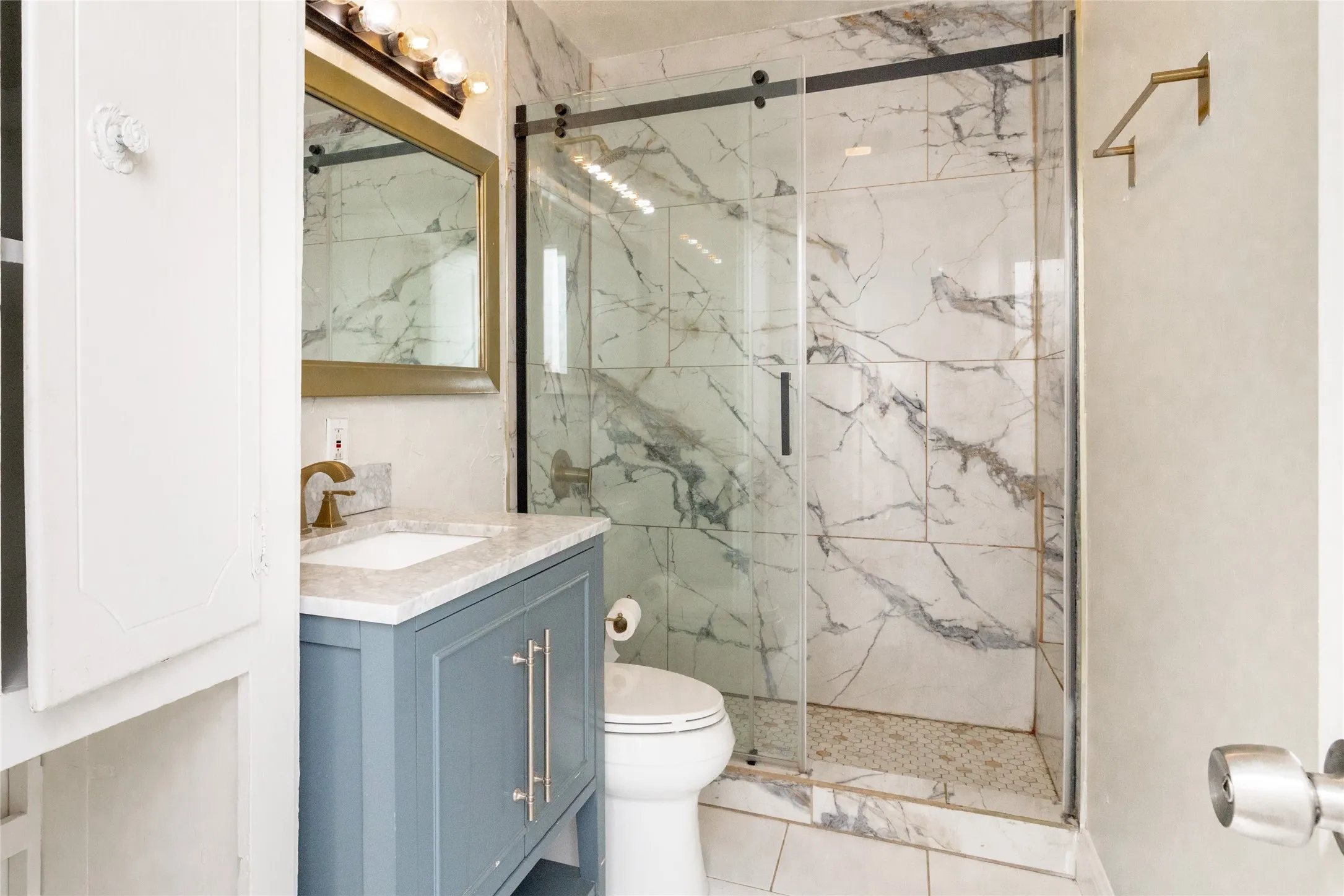 Walk-in shower with clear glass enclosure, marble-style tile surround, and mosaic tile flooring