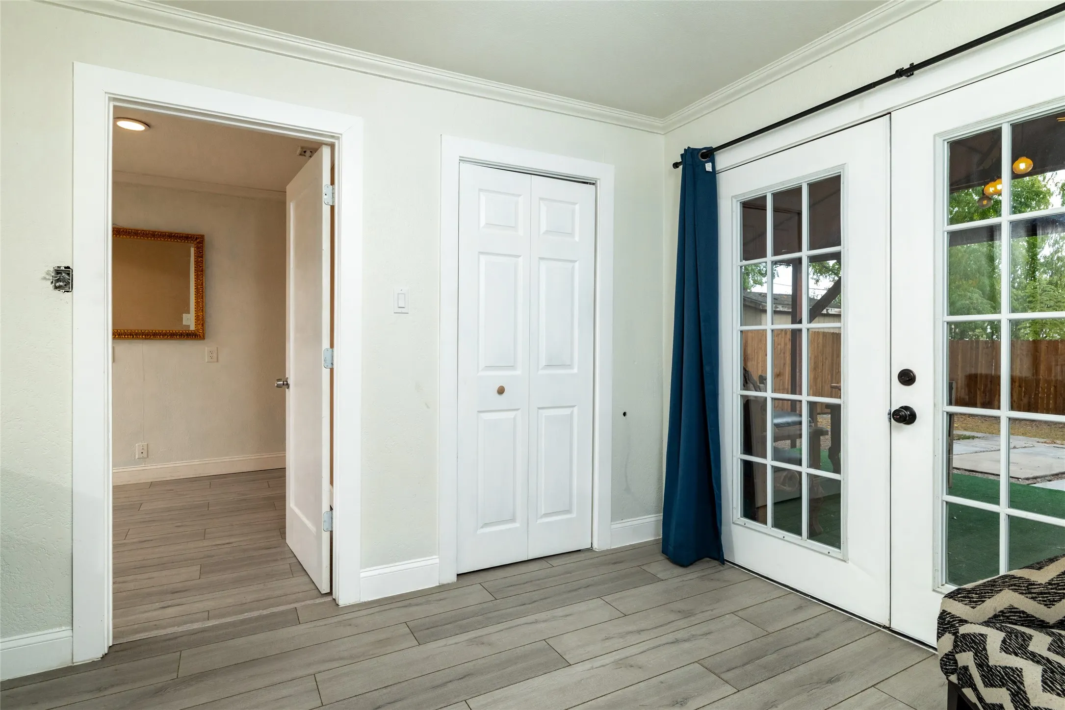Wood-finish flooring throughout, white interior walls, white trim, white paneled bifold closet door, and white French doors with divided lites