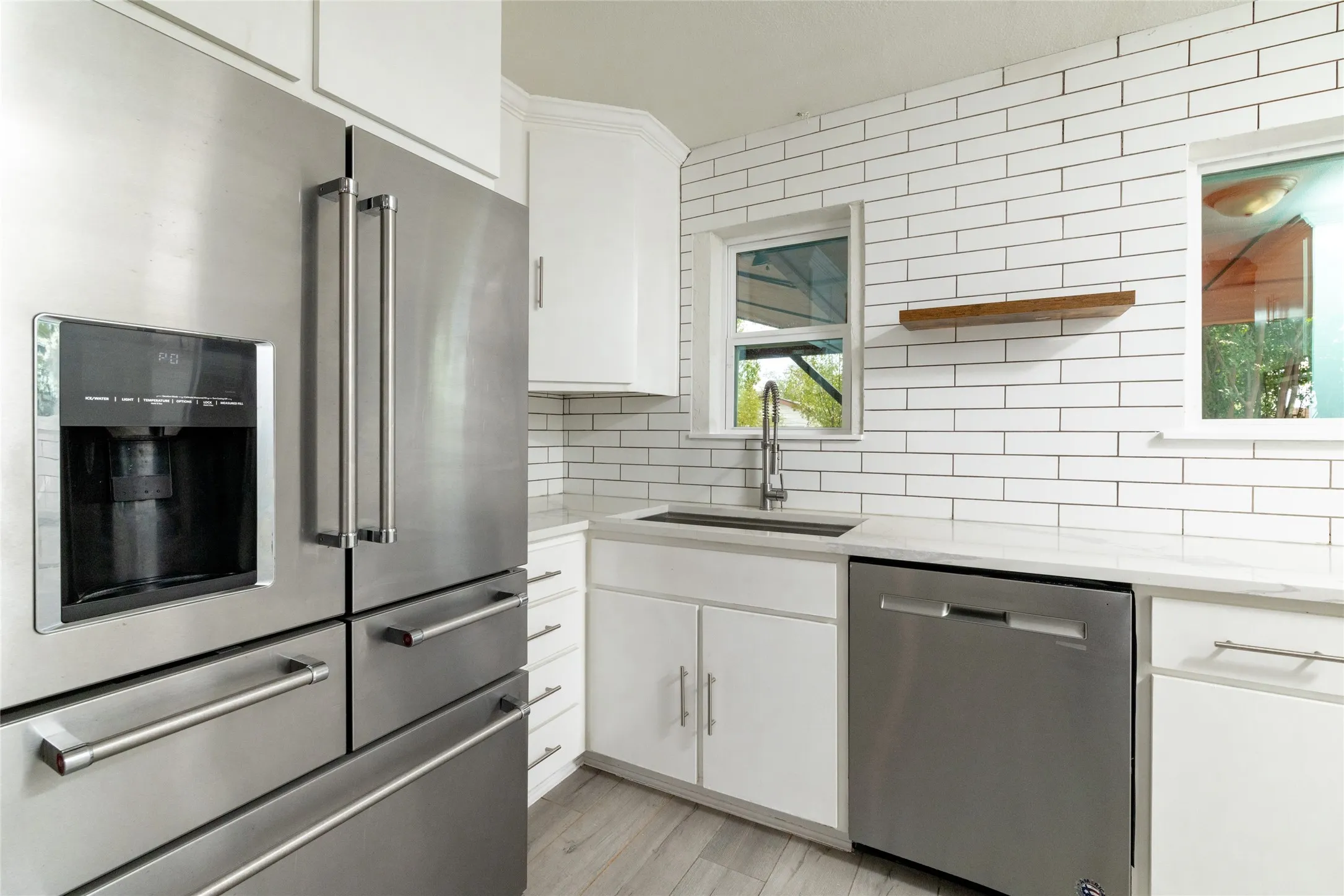 Stainless steel French door refrigerator, white subway tile backsplash, white countertops, stainless steel dishwasher, and wood-finish flooring