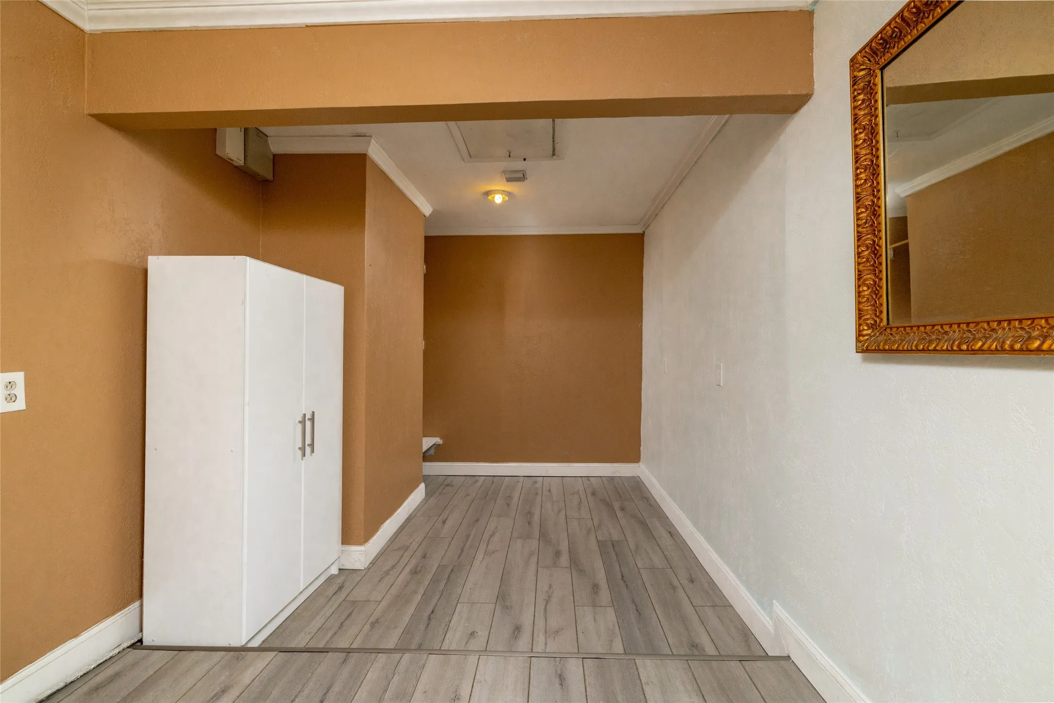 Wood-finish flooring with white trim, built-in white cabinetry, and overhead lighting