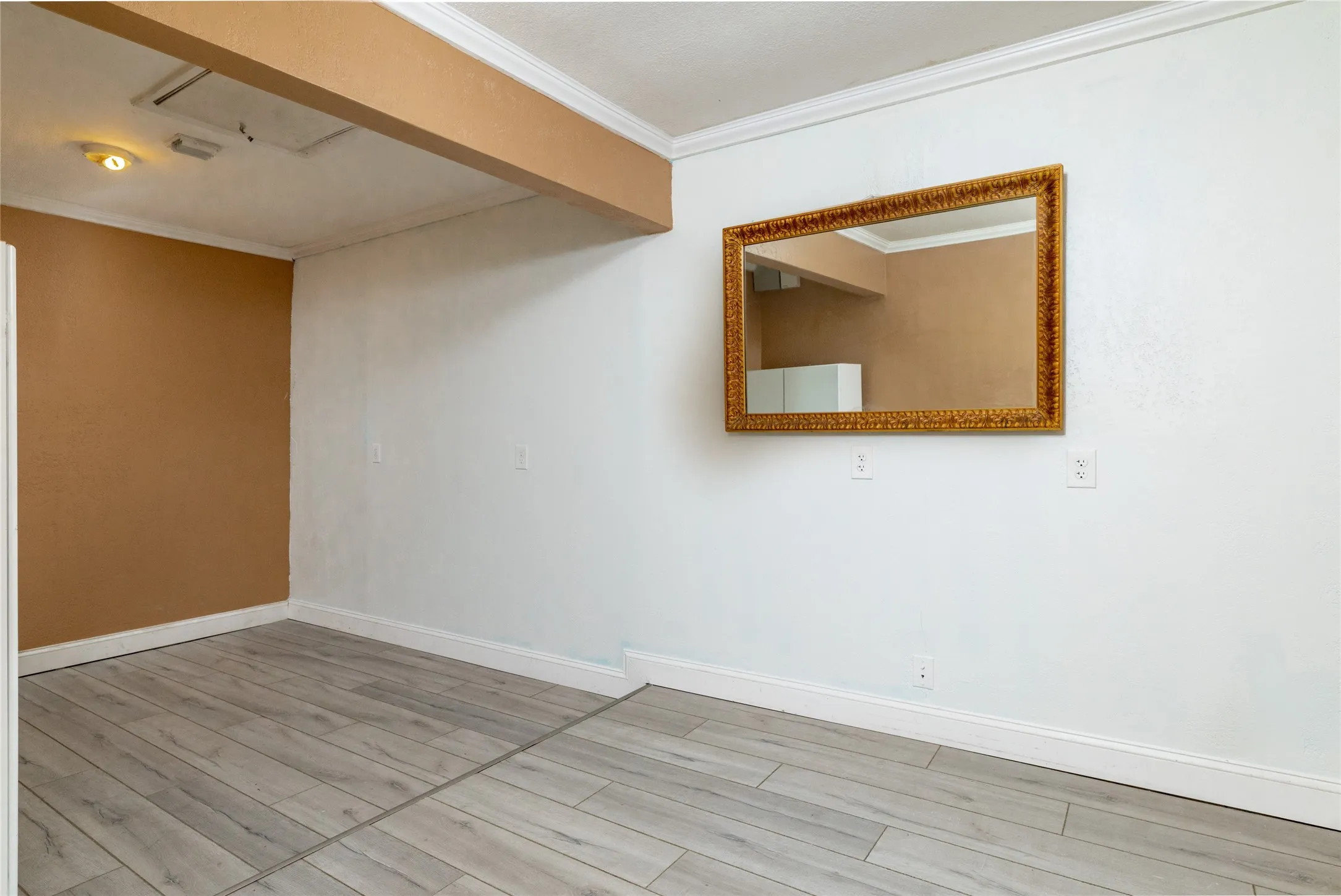 Wood-finish flooring with white baseboards and crown molding