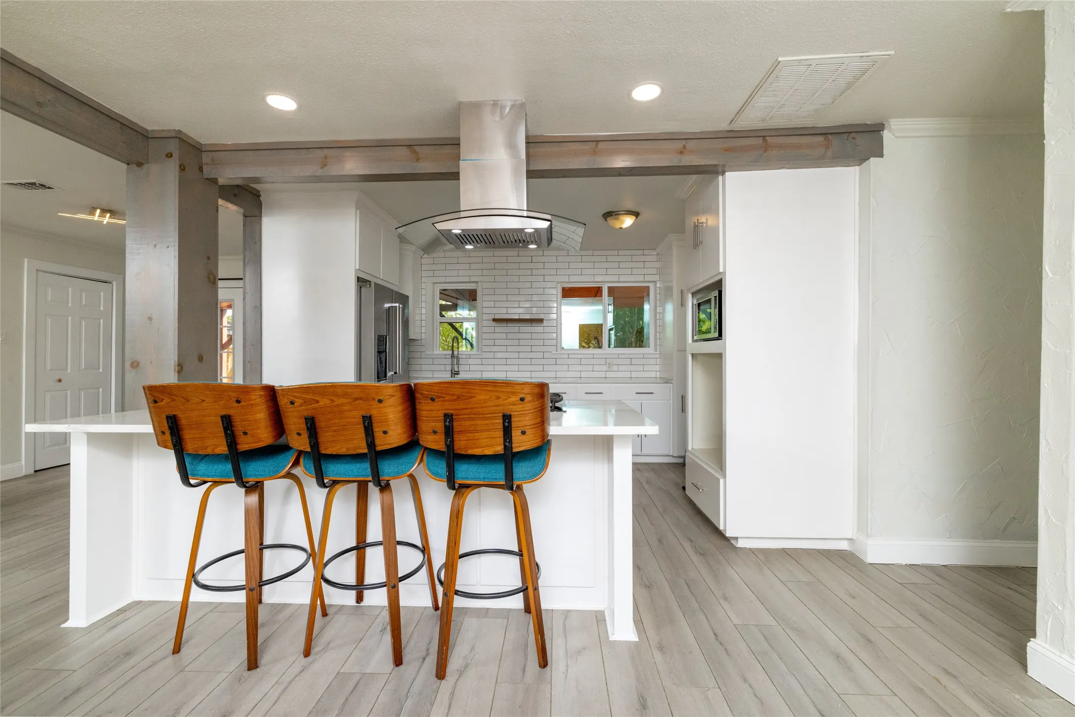 White kitchen island with countertop seating, wood-finish flooring, white subway tile backsplash, stainless steel range hood, and recessed lighting
