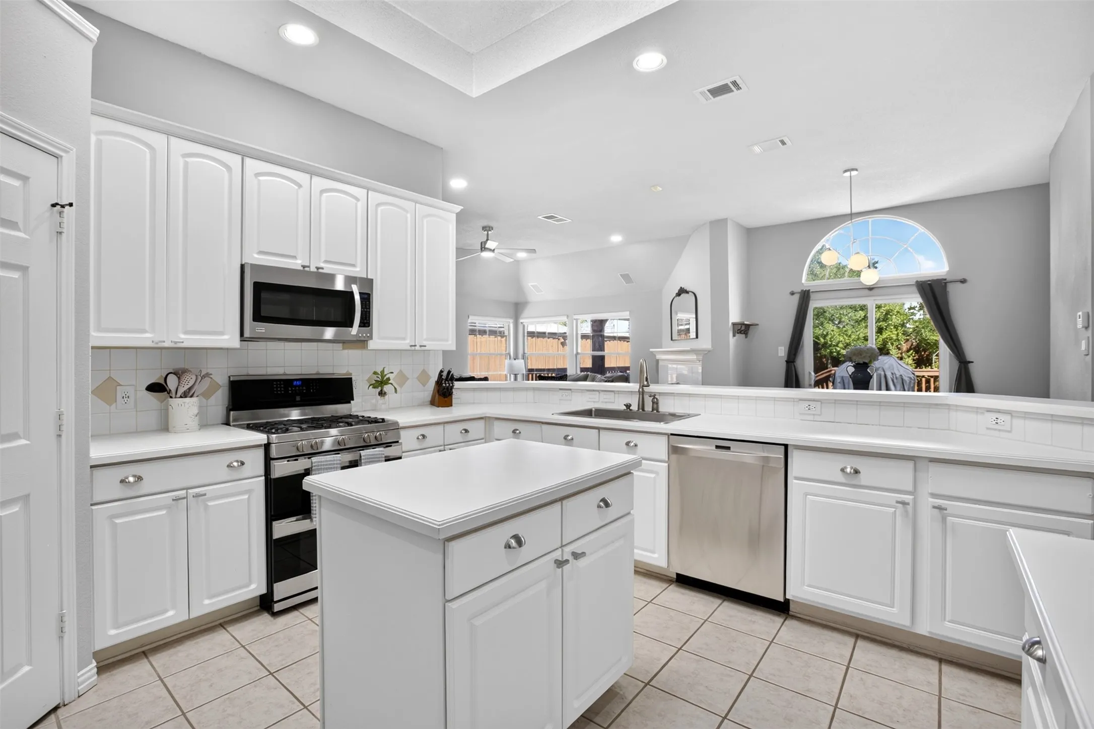 Recessed lighting, stainless steel appliances, central island, white cabinetry, and tile flooring