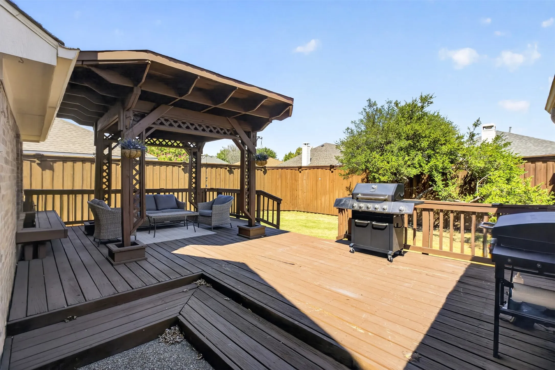 Expansive wood-finish deck featuring a built-in gazebo with lattice accents, multi-level design, and surrounding privacy fencing
