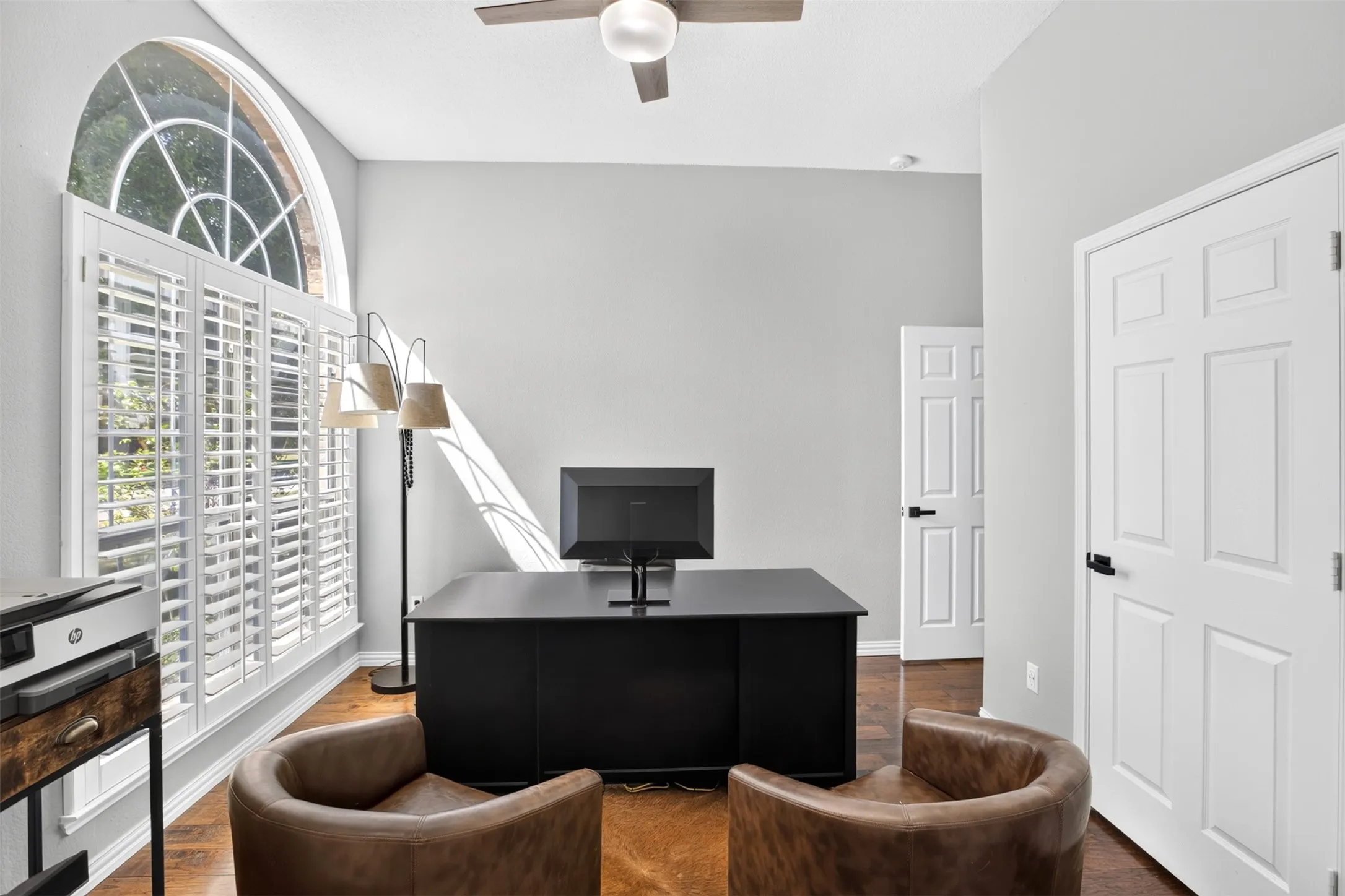 Arched transom window with plantation shutters, wood-finish flooring, ceiling fan, and paneled interior doors