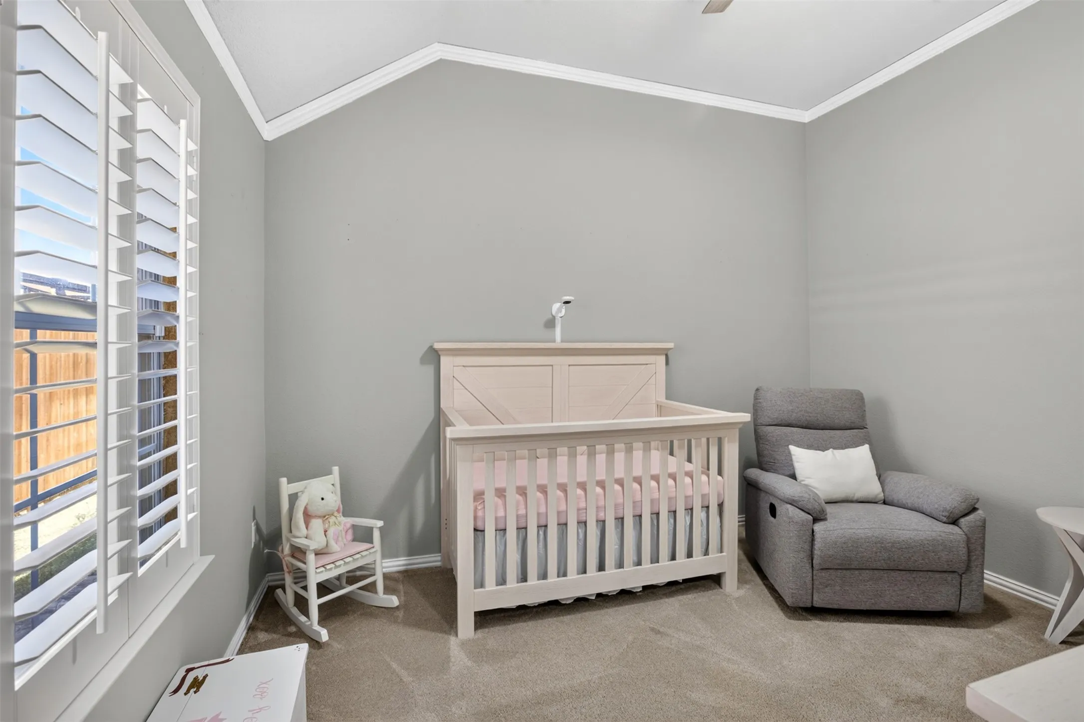 Vaulted ceiling with crown molding, plantation shutters, and neutral-toned wall paint