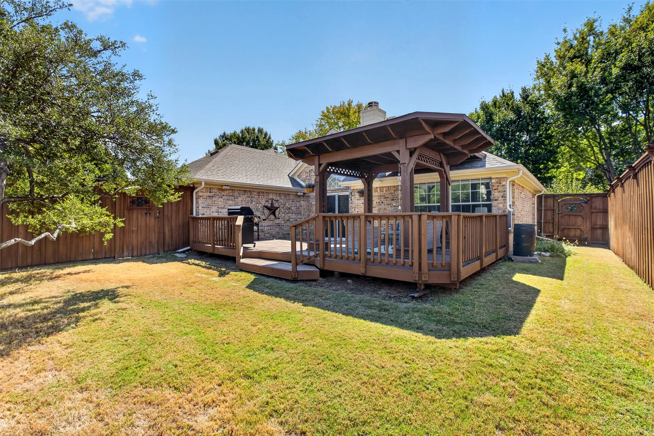 Expansive backyard featuring a wood deck with a gazebo, mature trees, and privacy fencing