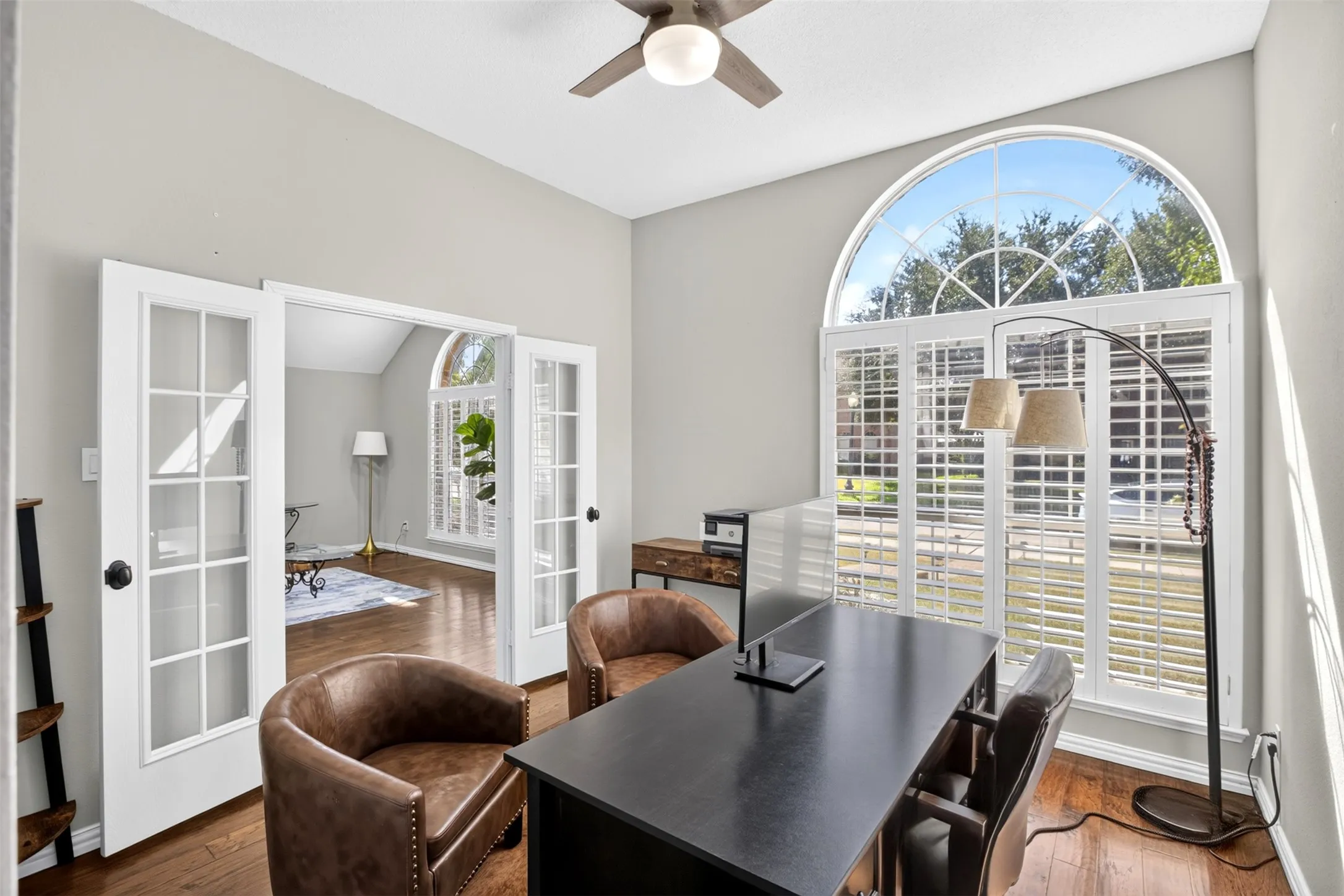 Arched window with plantation shutters, wood-finish flooring, ceiling fan, and double French doors with glass panels
