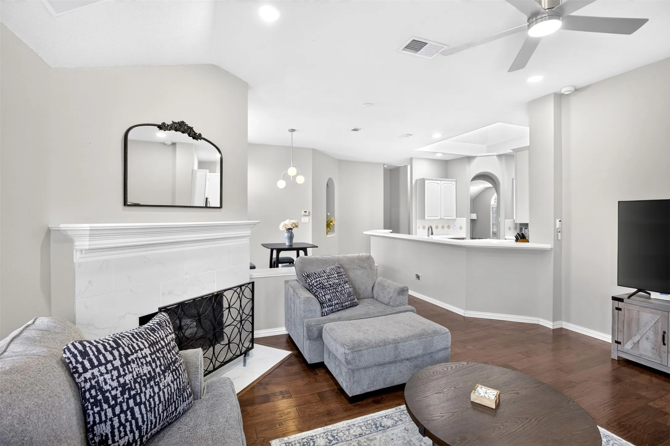 Open-concept living area with dark wood-finish flooring, a white mantel fireplace, vaulted ceilings, and a ceiling fan
