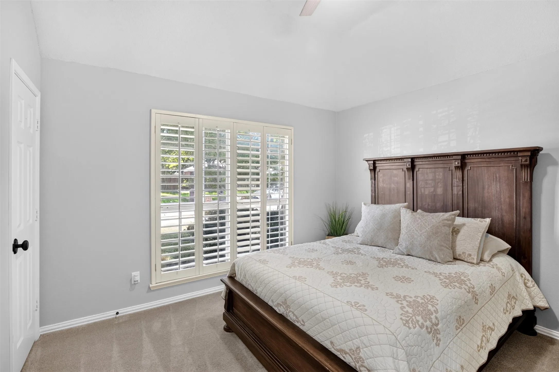 Vaulted ceiling with a ceiling fan, white paneled door with black hardware, large window with white plantation shutters, and light gray wall paint
