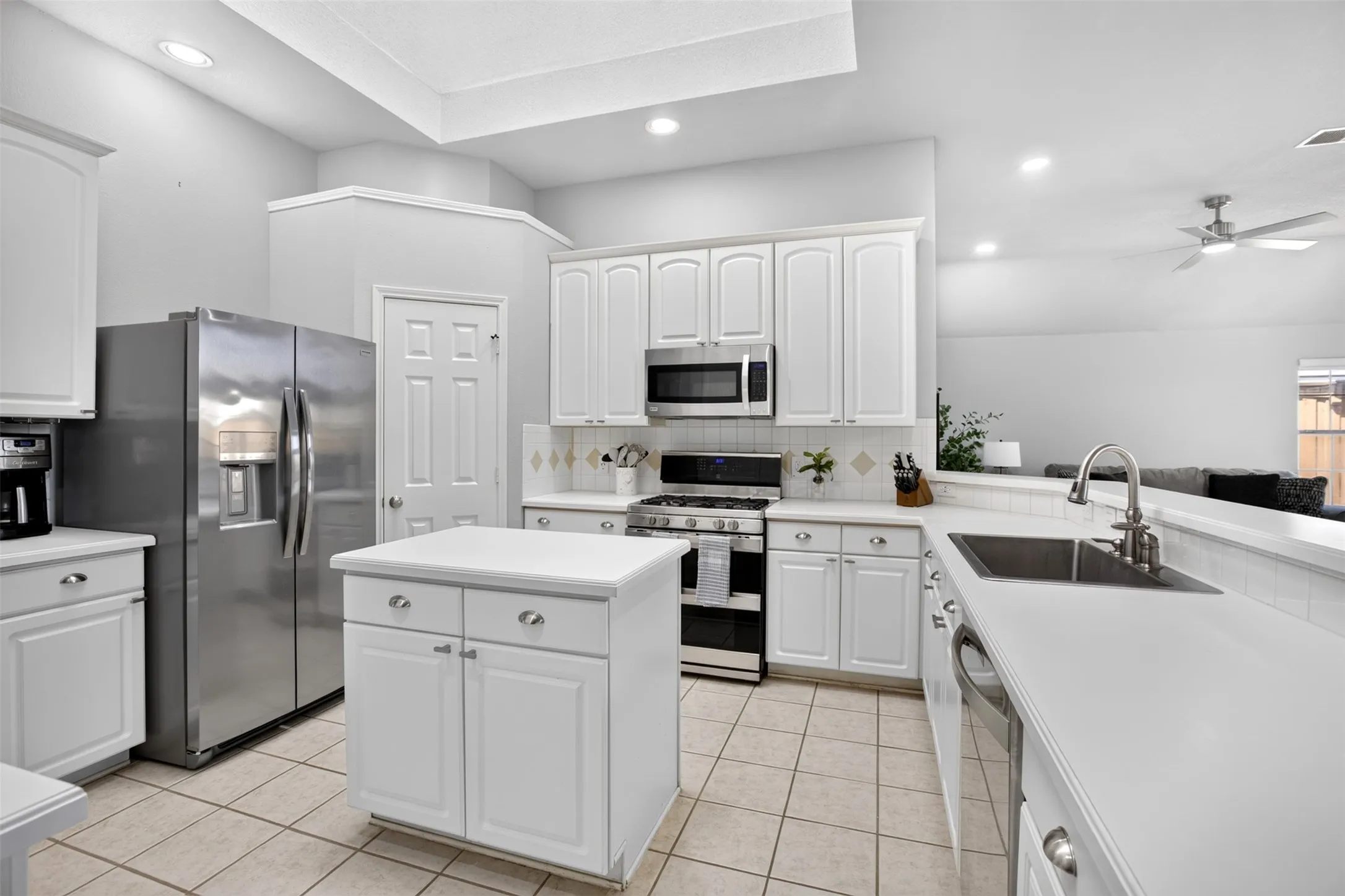White cabinetry, stainless steel appliances, central island, tile flooring, and recessed lighting