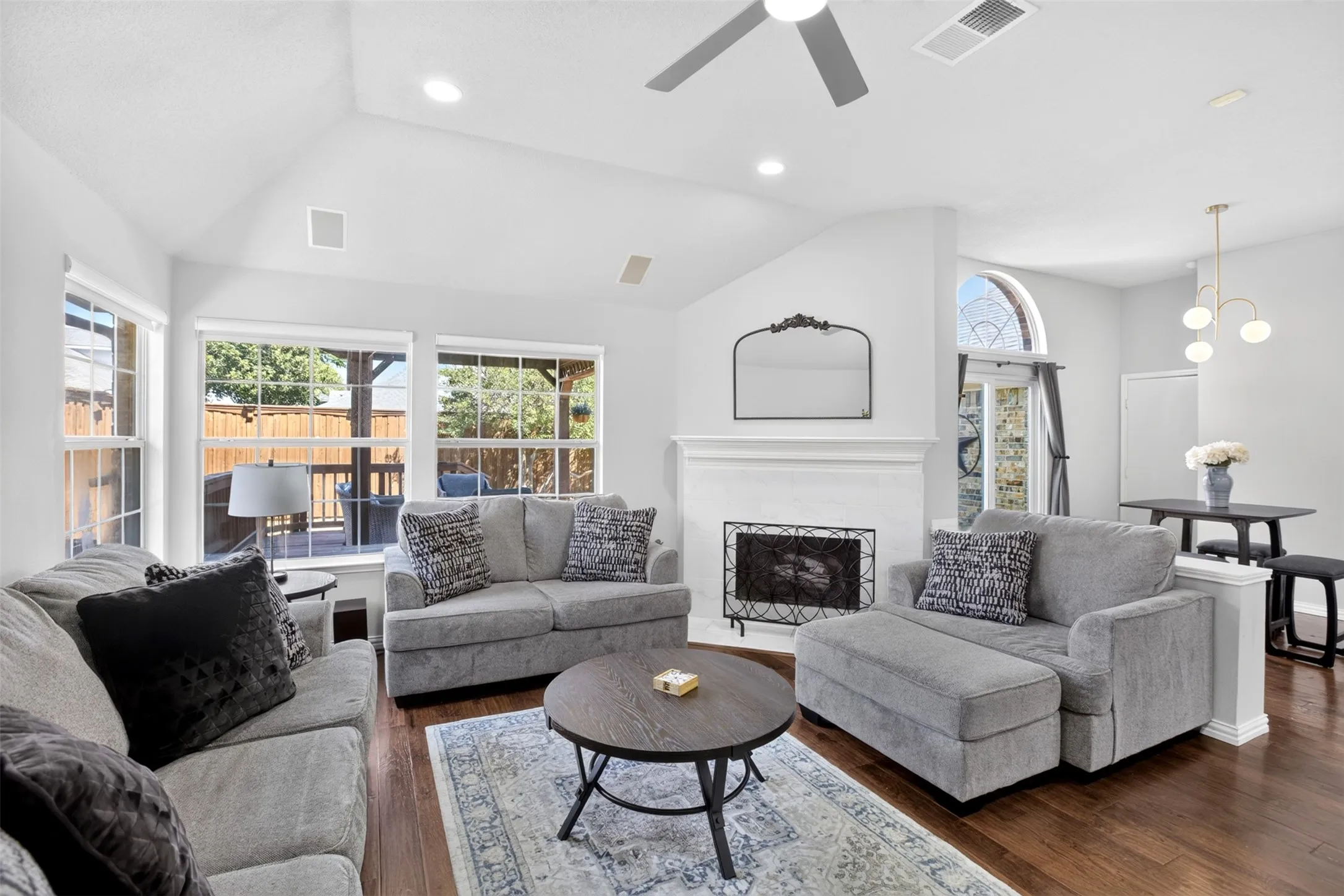 Vaulted ceiling, recessed lighting, wood-finish flooring, white brick fireplace, and backyard access