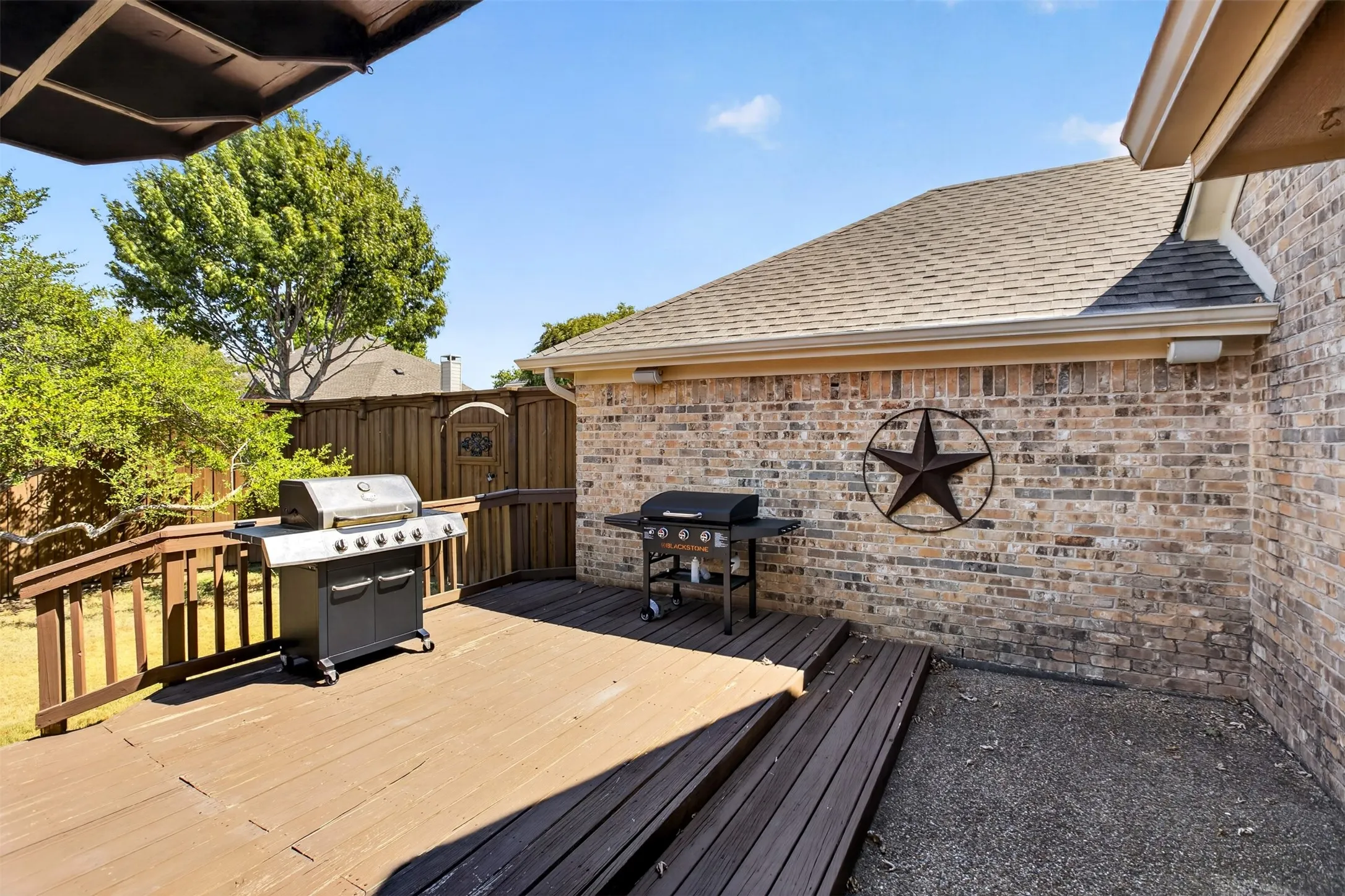 Expansive wood-finish decking with handrails, brick exterior, and a privacy fence