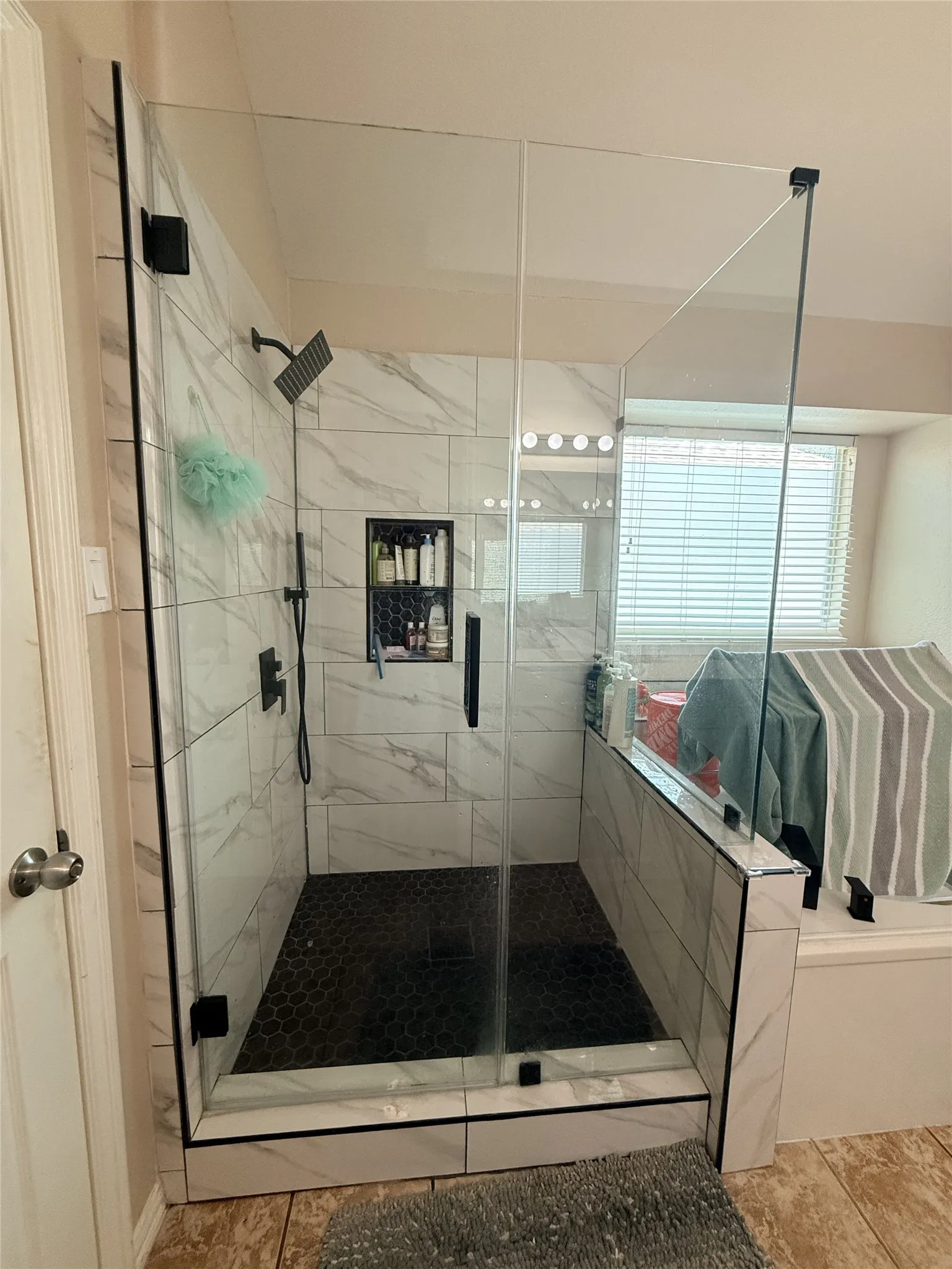 Glass-enclosed shower with black hexagonal tile flooring and white marble-look wall tile