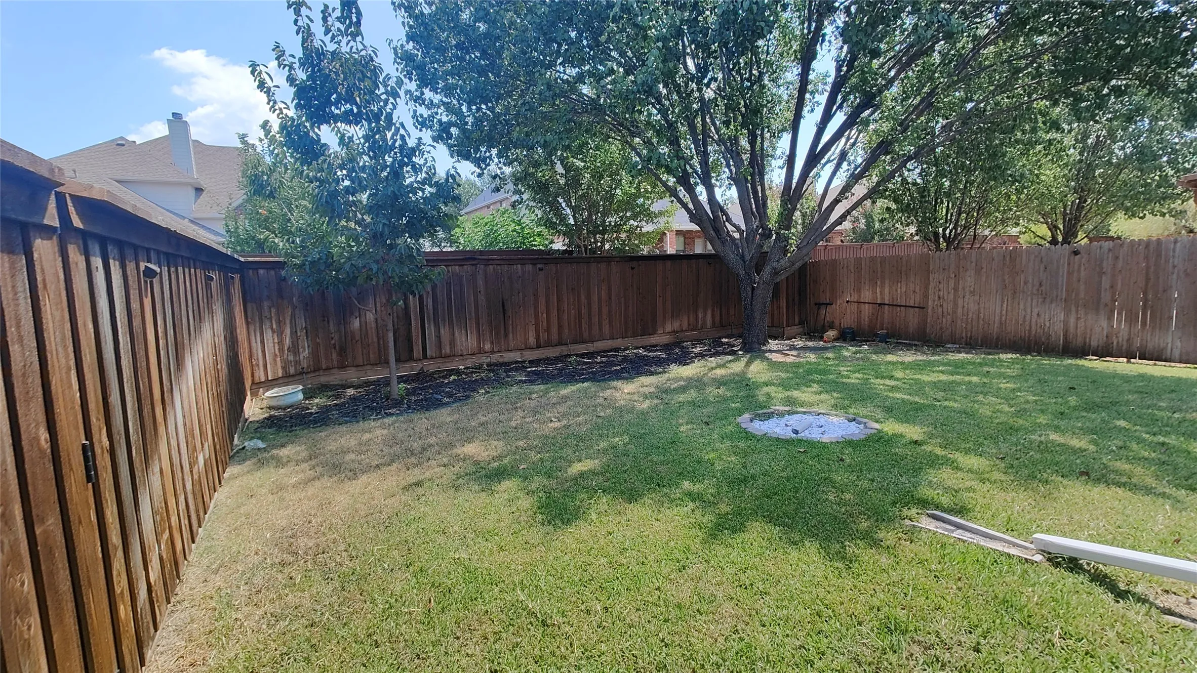 Fenced backyard featuring mature trees and a manicured lawn