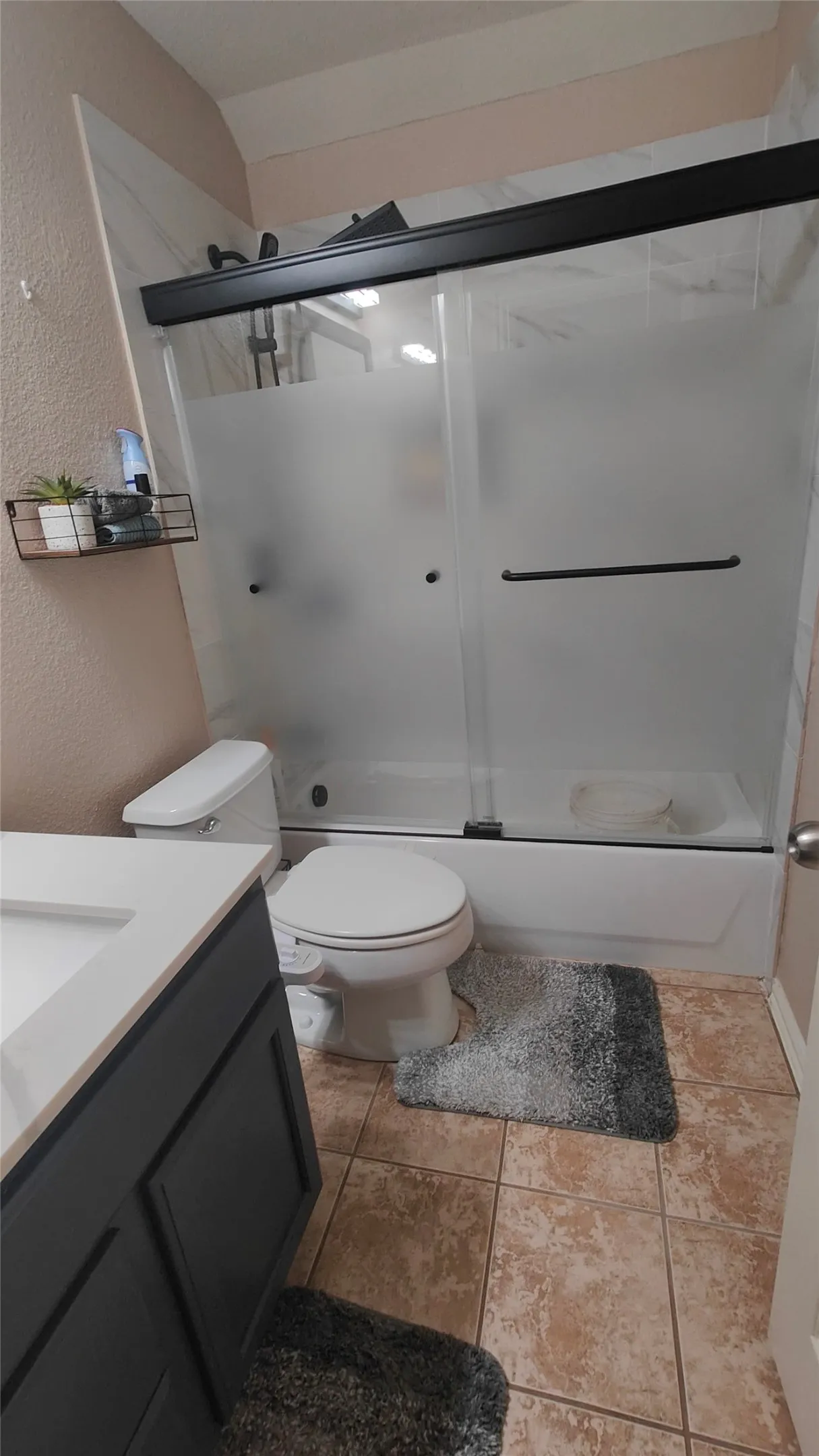 Built-in vanity with integrated sink, coordinating toilet, and a combination shower/bathtub with sliding frosted glass doors