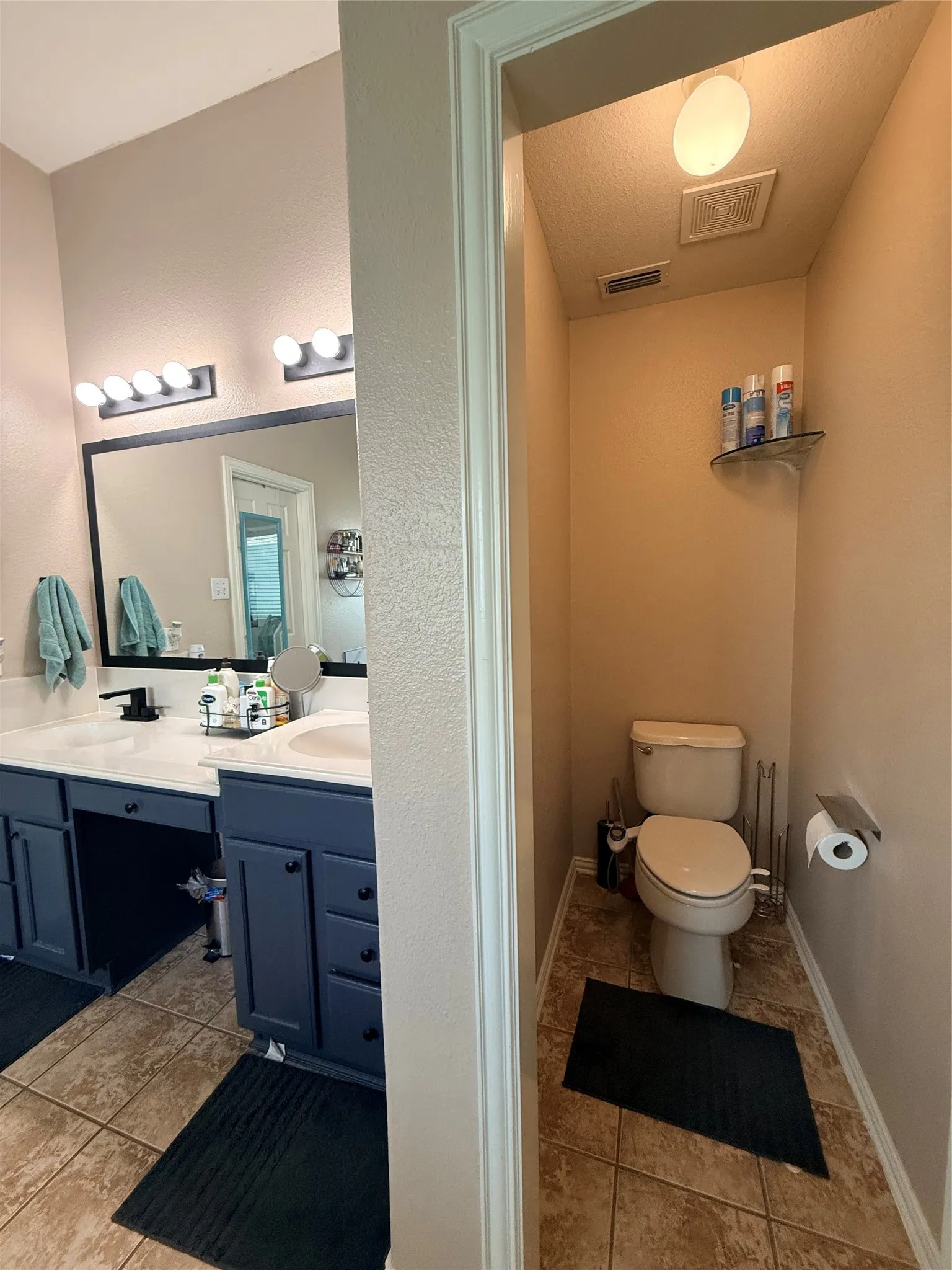 Dual vanity with white countertops and dark blue cabinetry, featuring a large mirror with integrated lighting