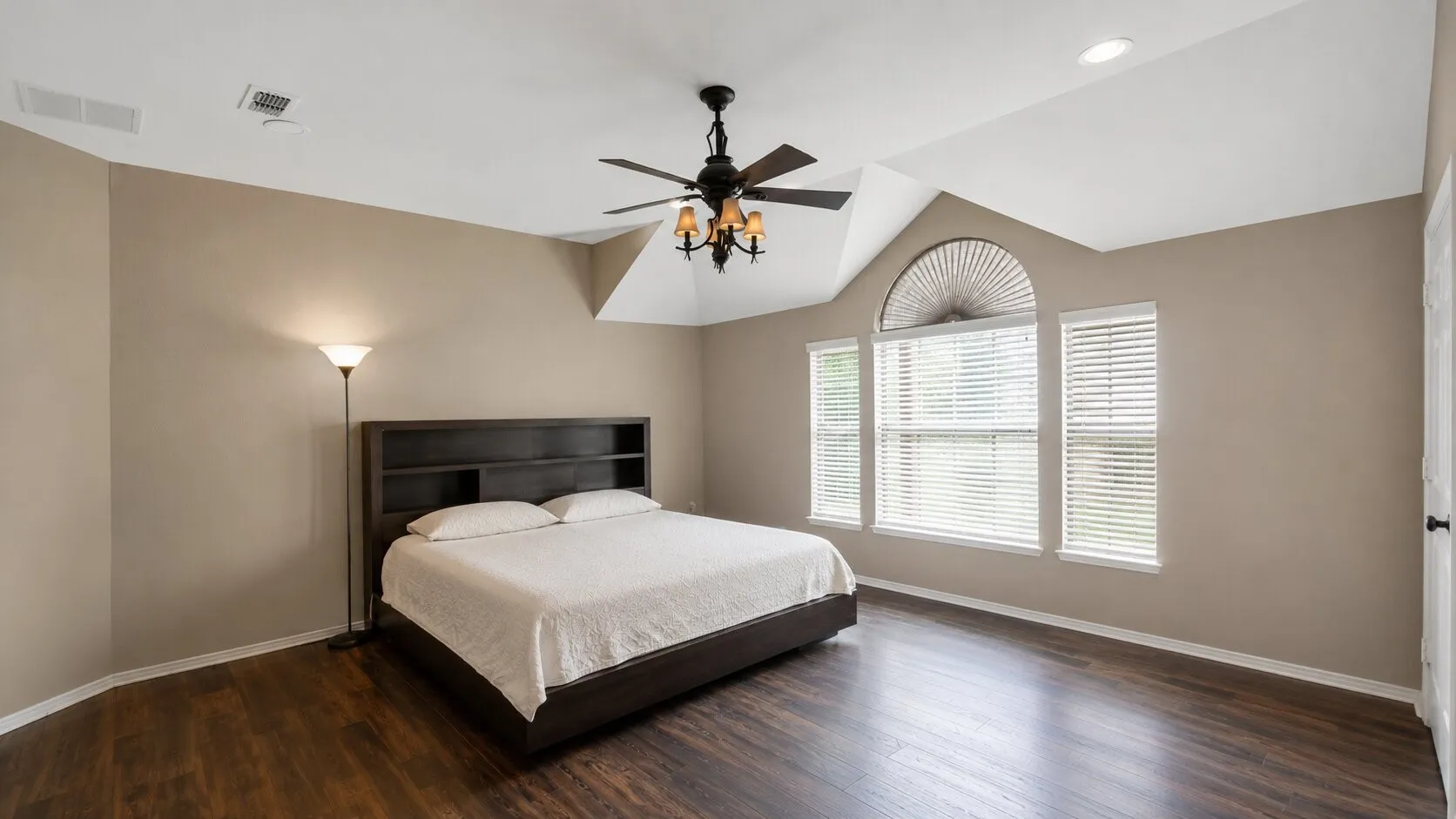 Vaulted ceiling with a ceiling fan light fixture, wood-finish flooring, and arched window with two rectangular windows