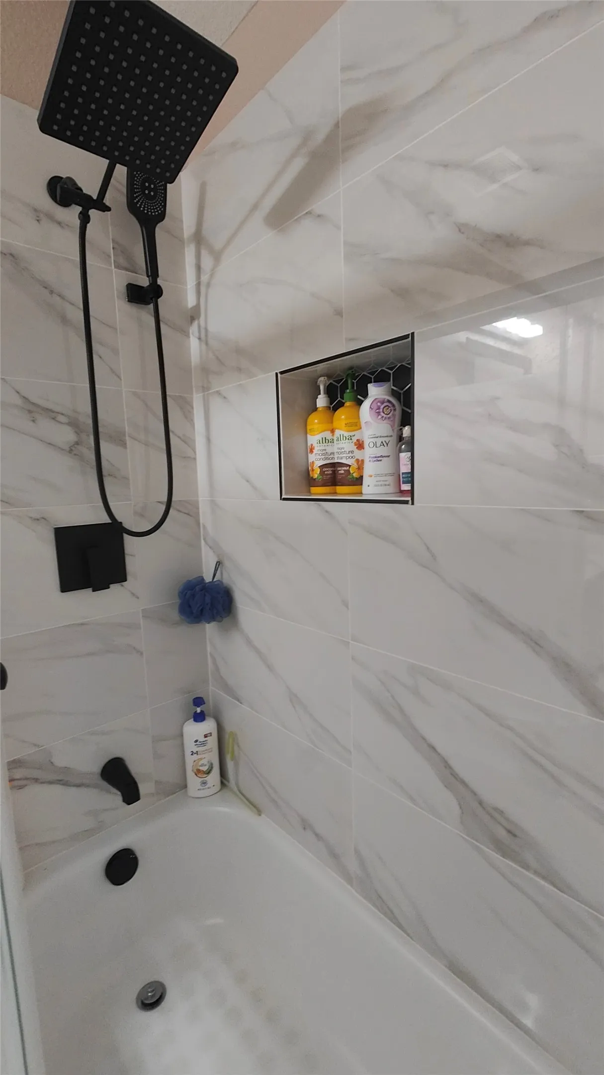 Bathtub with white subway tile surround, black shower fixtures, and a recessed shower niche with hexagonal tile