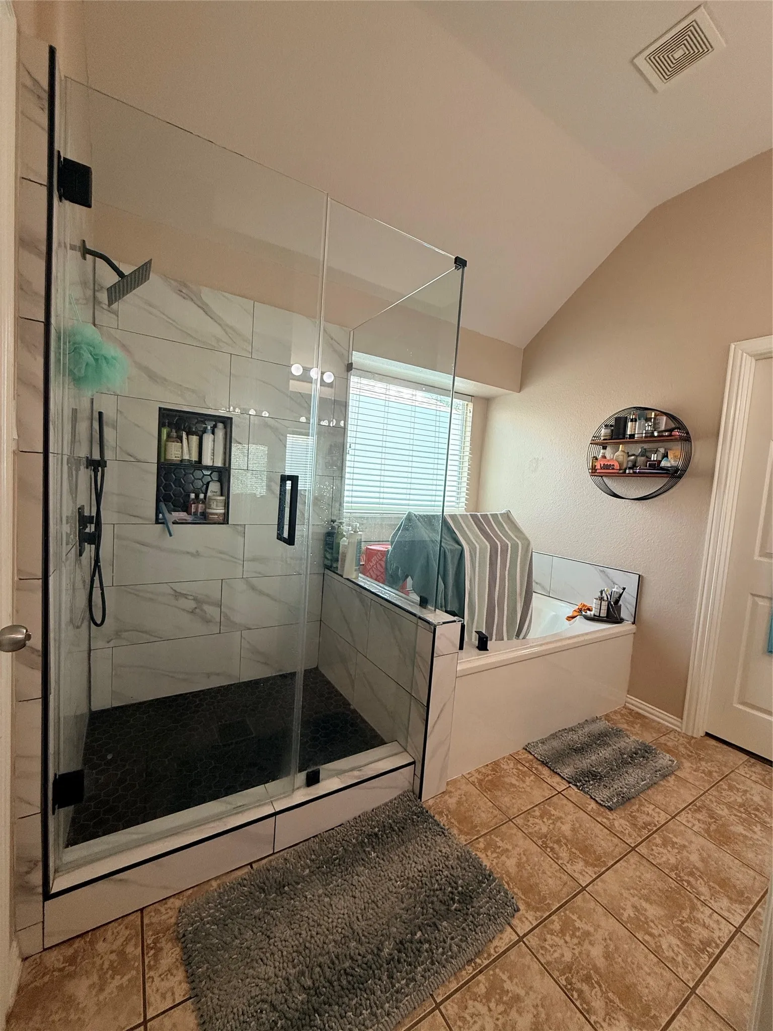 Glass-enclosed shower with a rainfall showerhead, tiled accent niche, and dark hexagonal tile flooring