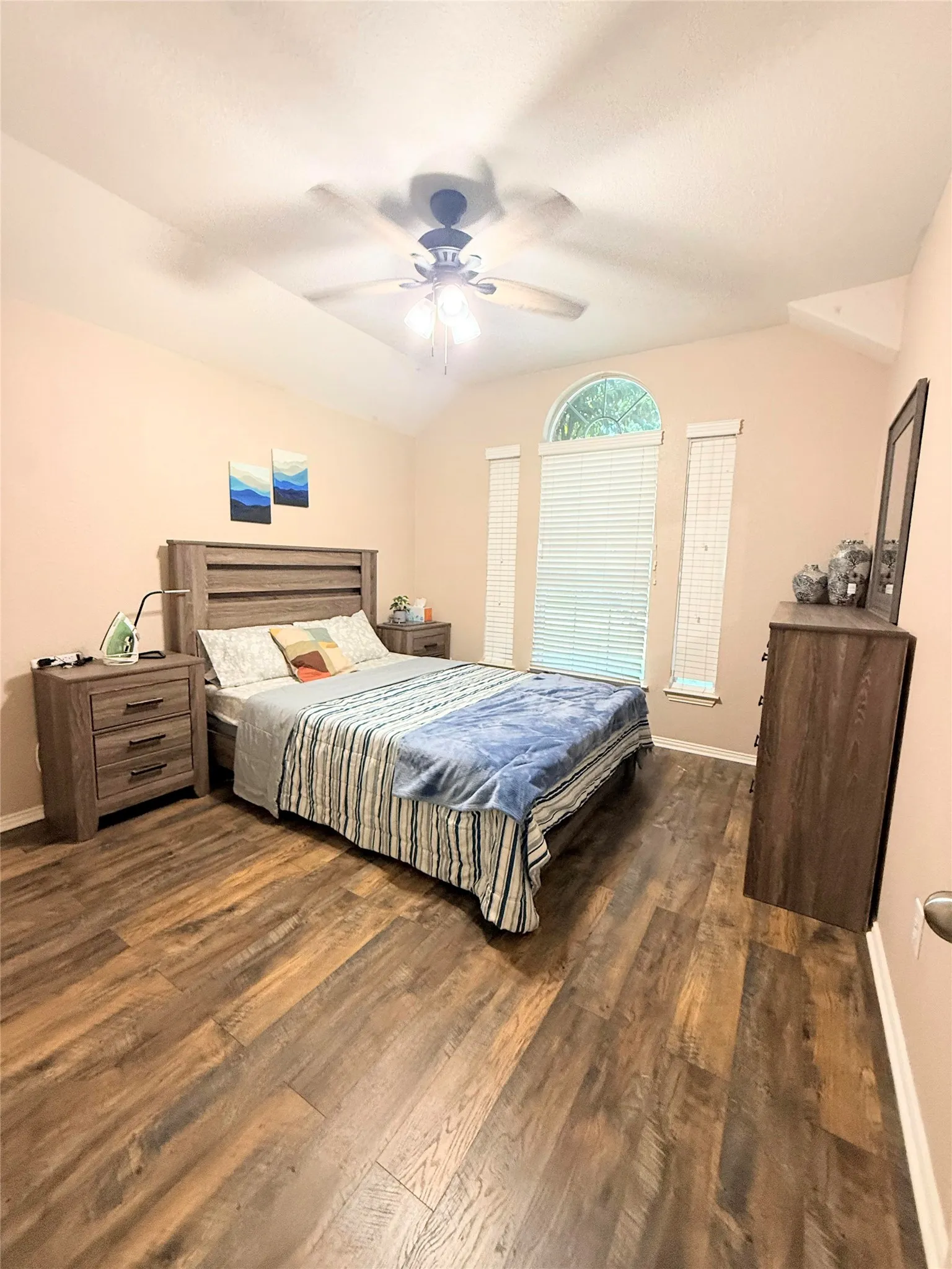 Vaulted ceiling with a ceiling fan, wood-finish flooring, and arched window with blinds