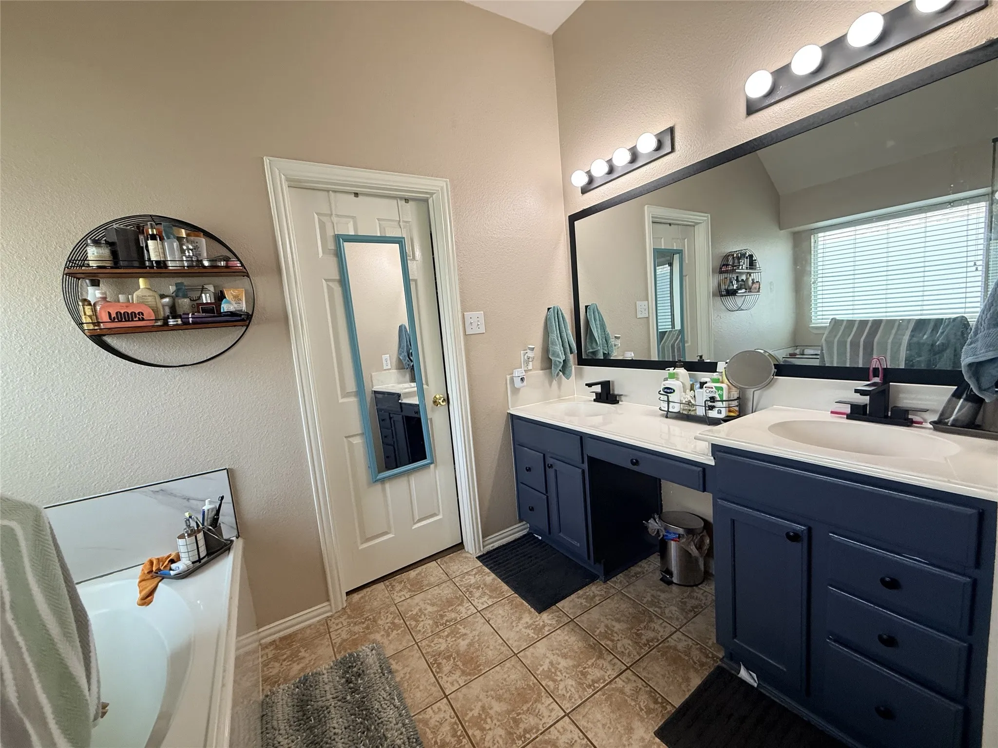Dual vanity with integrated sinks and dark cabinetry, large wall-mounted mirror, overhead vanity lighting, and ceramic tile flooring