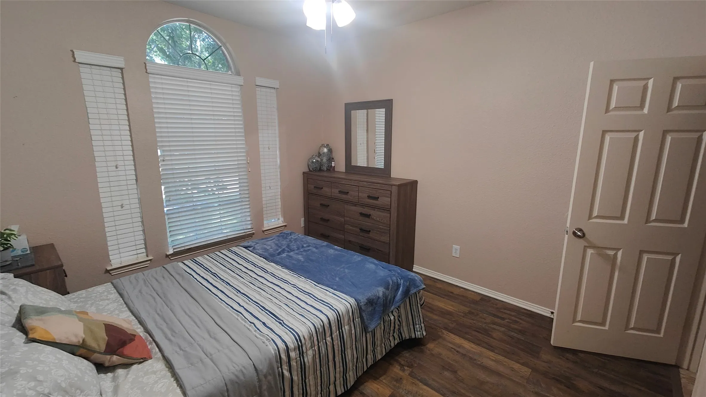 Wood-finish flooring, ceiling fan with light fixture, and arched window with blinds
