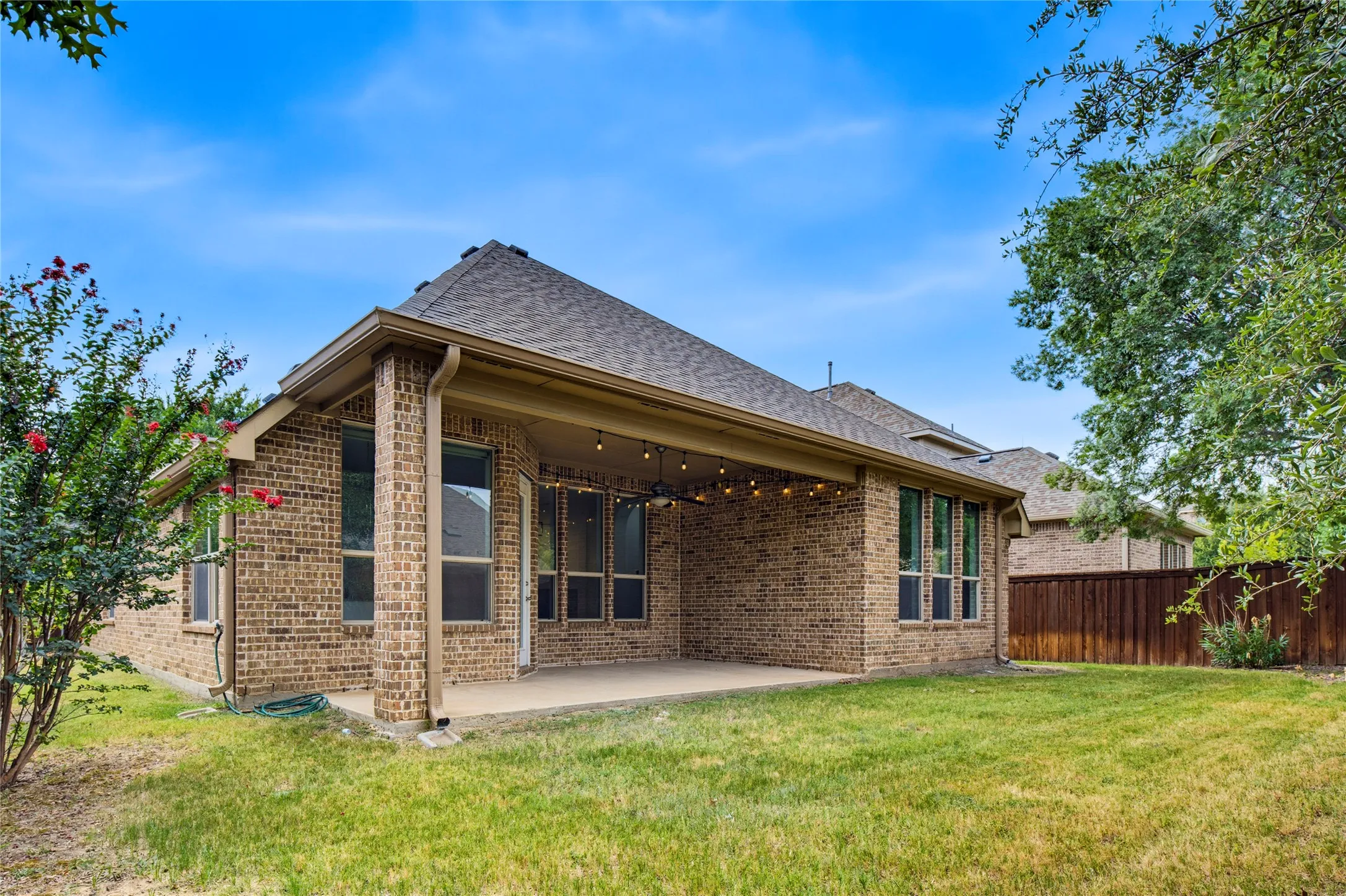 Brick exterior with a covered patio, extensive windows, and a shingle roof