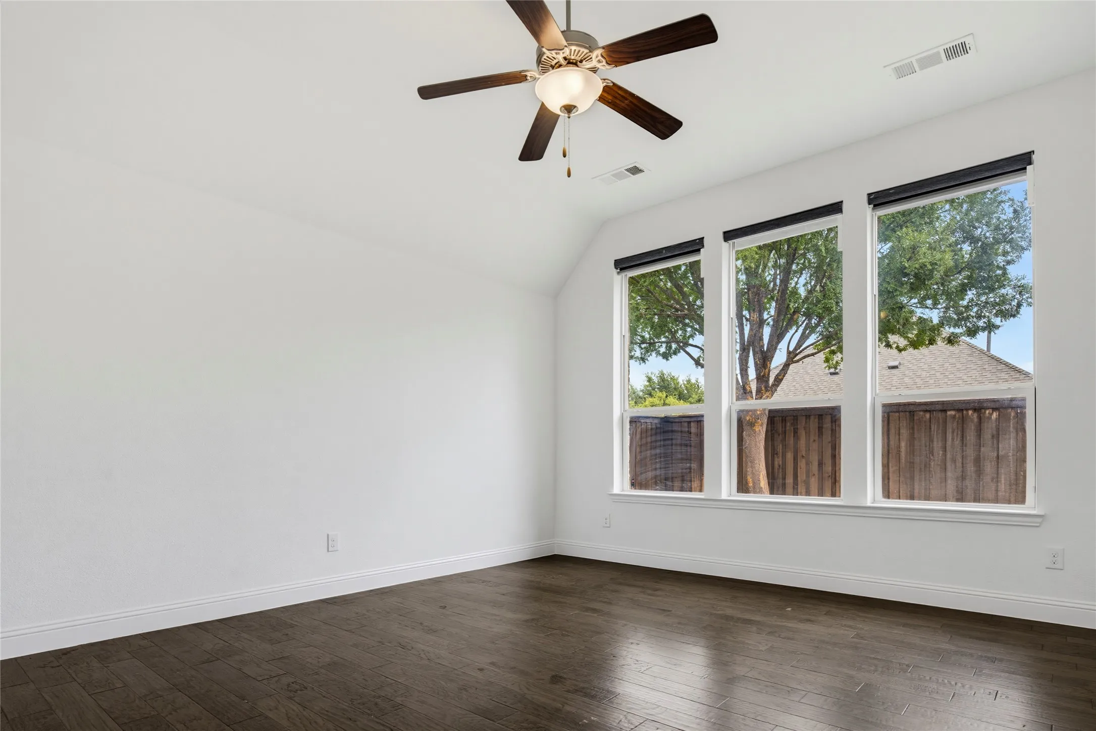 Bright interior with three large windows, wood-finish flooring, a ceiling fan with integrated lighting, and white walls