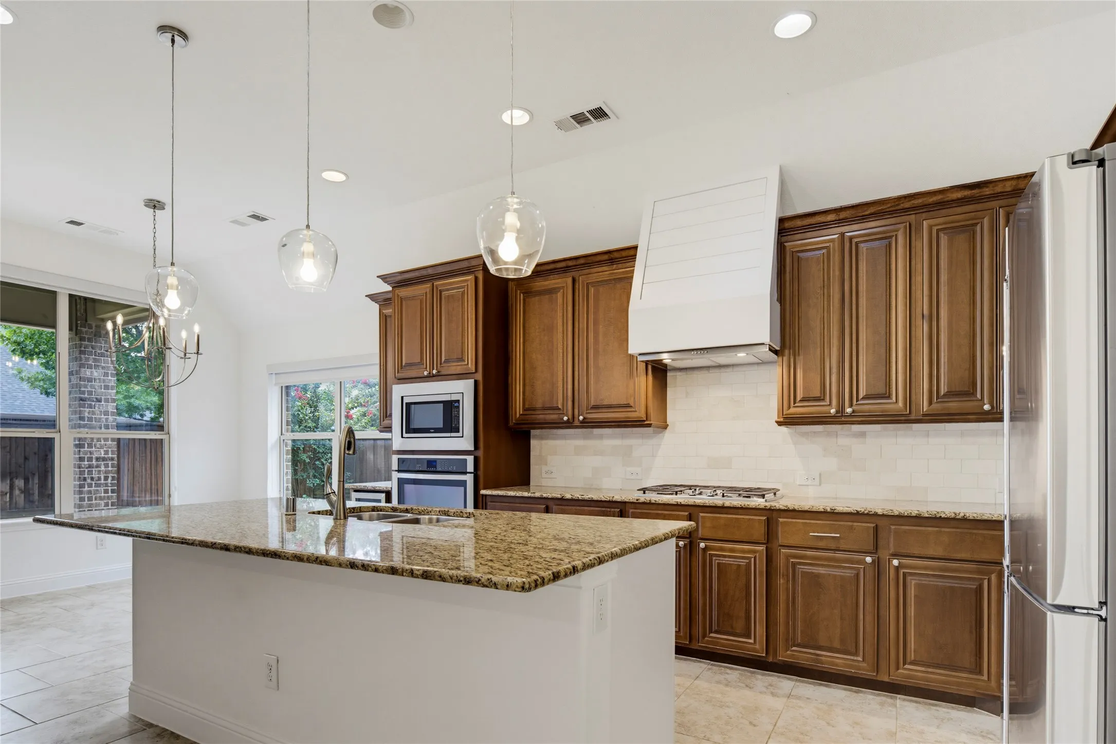 Kitchen featuring warm wood cabinetry, granite countertops, stainless steel appliances, a subway tile backsplash, and a large center island with a sink