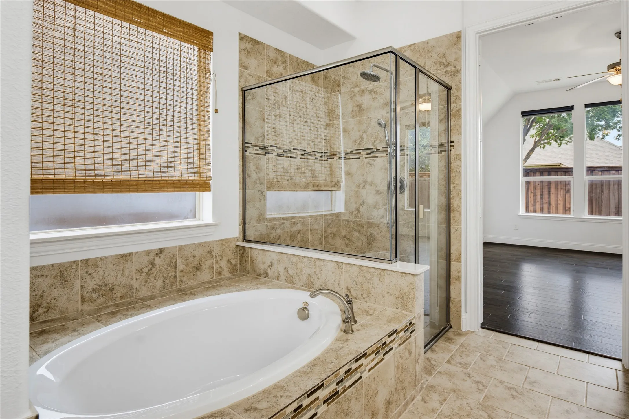 Soaking tub with a deck-mounted faucet, tile surround, and glass-enclosed shower featuring a tiled niche