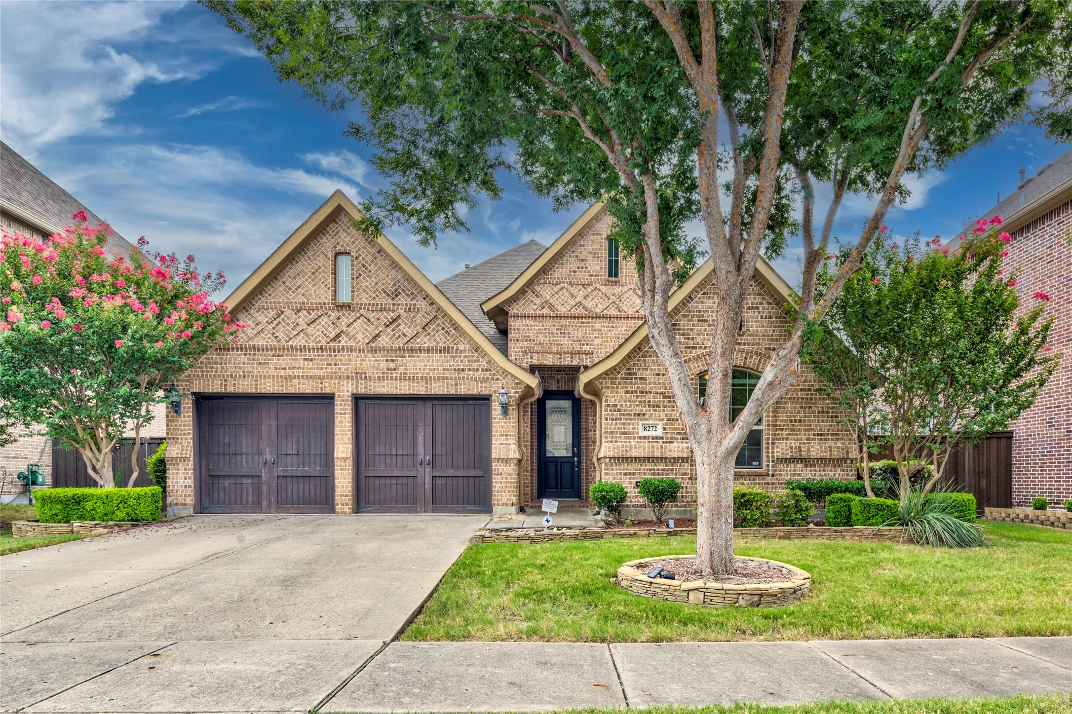 Brick exterior with gabled roof lines, attached two-car garage, concrete driveway, and established landscaping