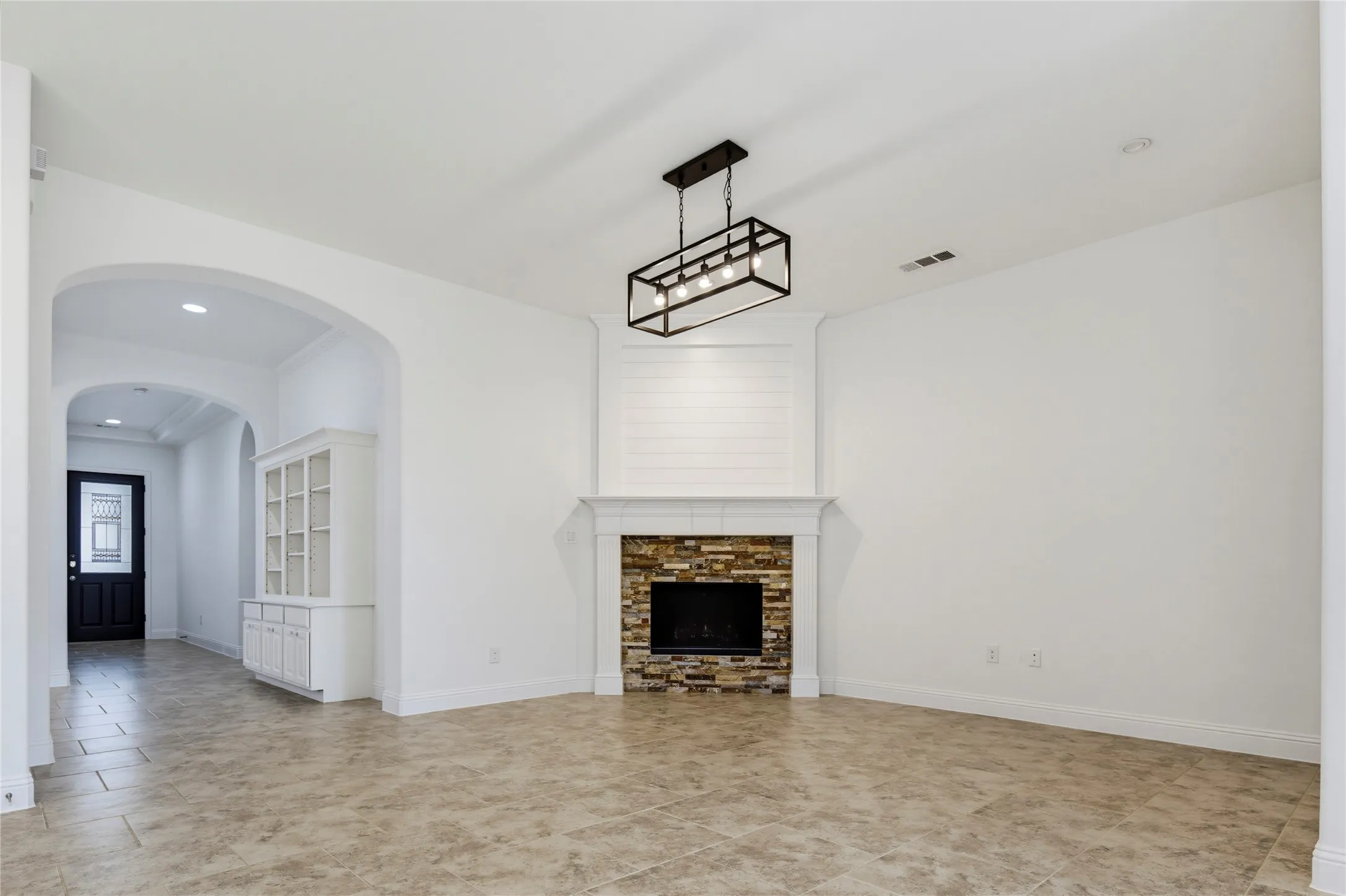 Stone-surround fireplace with a shiplap accent wall, an industrial-style chandelier, and tiled flooring