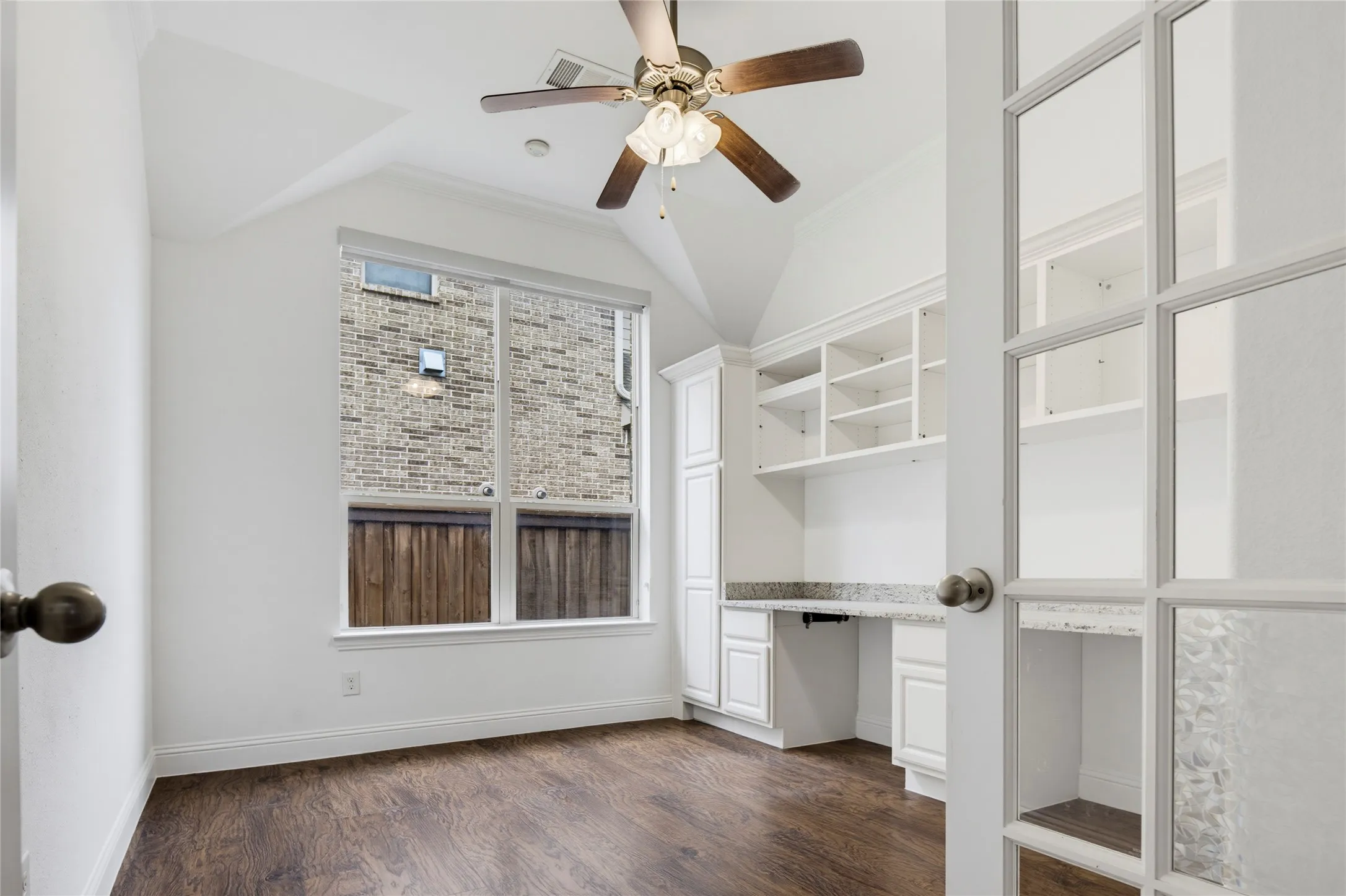 Wood-finish flooring, built-in desk with stone countertop, white built-in shelving, vaulted ceiling, and ceiling fan