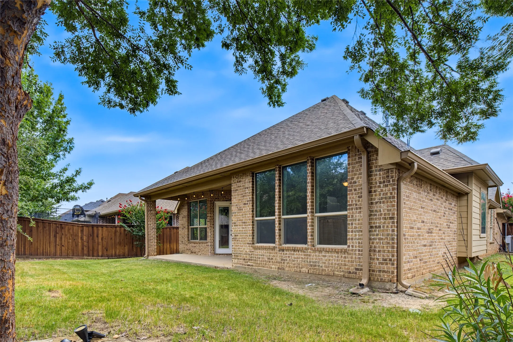 Brick exterior with a covered patio, multiple large windows, and a full privacy fence