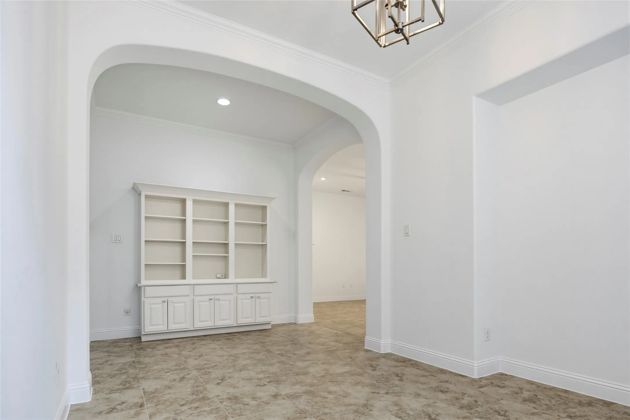 Recessed lighting, built-in shelving with cabinetry, crown molding, and arched doorways complement the tile flooring