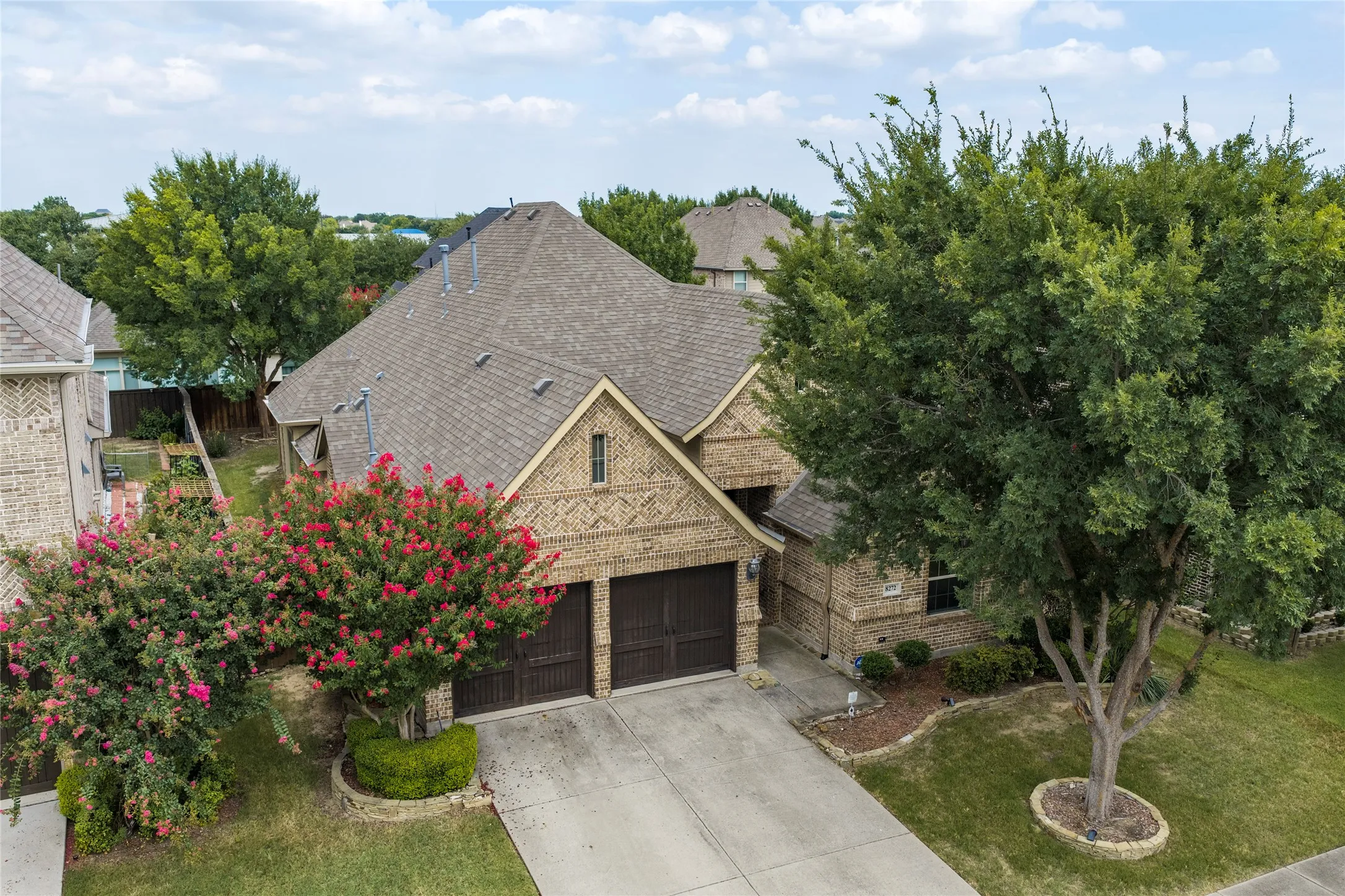 Brick exterior with a gabled roofline, two-car garage, concrete driveway, and established landscaping