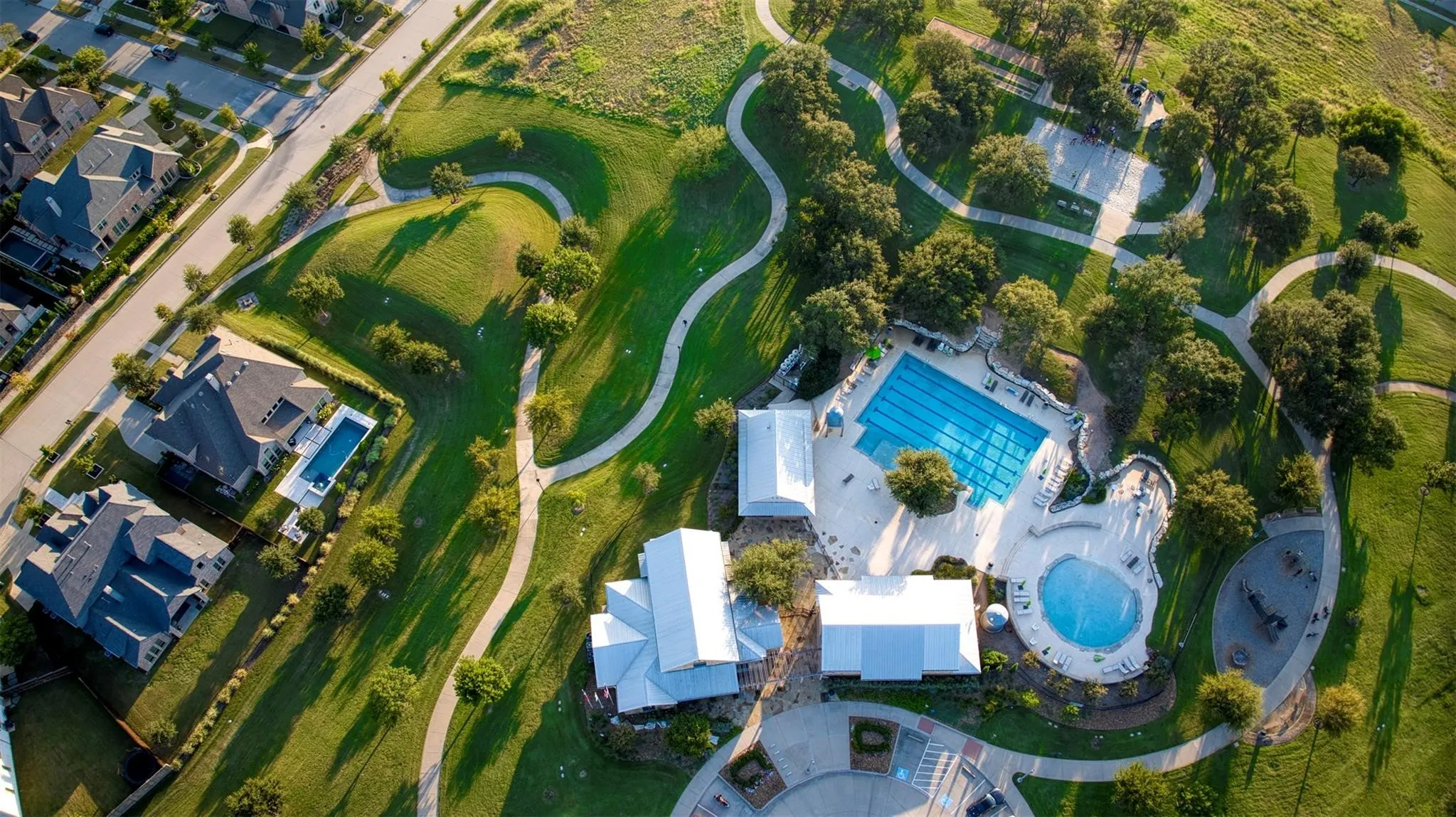 Aerial perspective showcasing a residential community with winding pathways, mature trees, and a central aquatic facility featuring a lap pool and a leisure pool