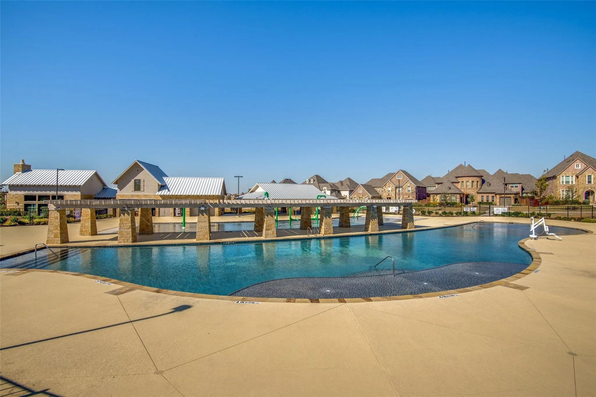 Expansive community pool with a sun shelf, adjacent shallow water play area, and stone-columned pergola