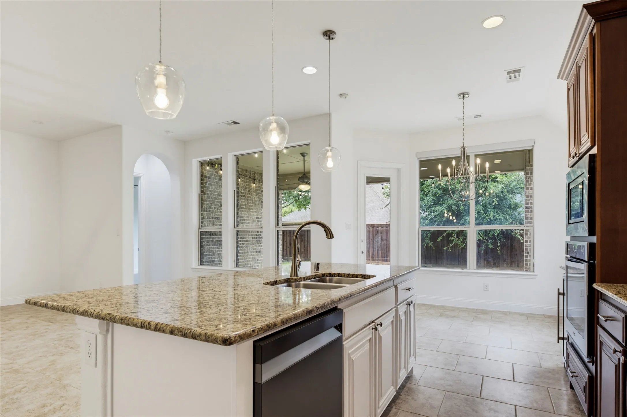 Kitchen island with a light-toned stone countertop, integrated double basin sink, and pendant lighting